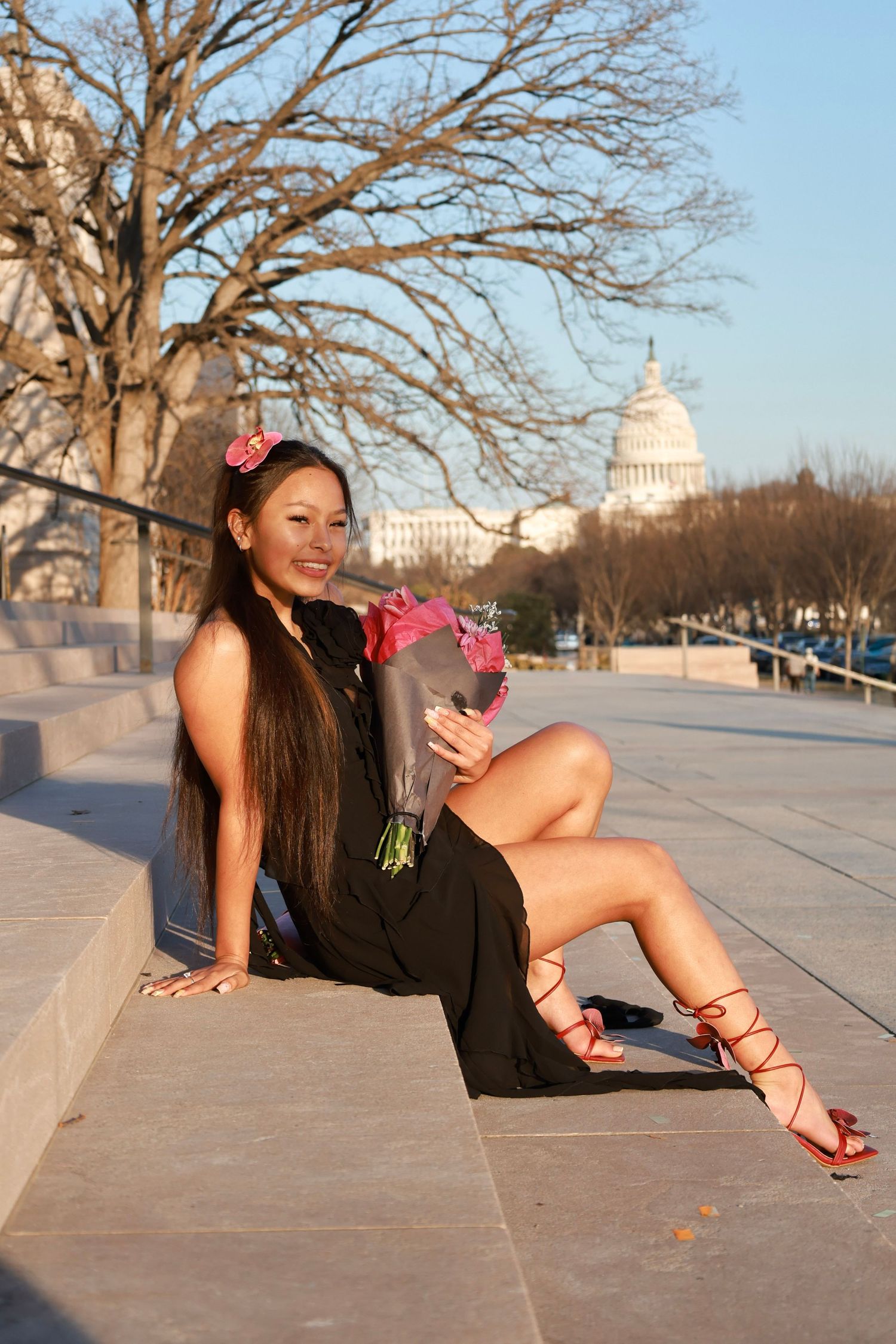 Young woman in black dress holds pink roses on steps near US Capitol building in Washington DC.