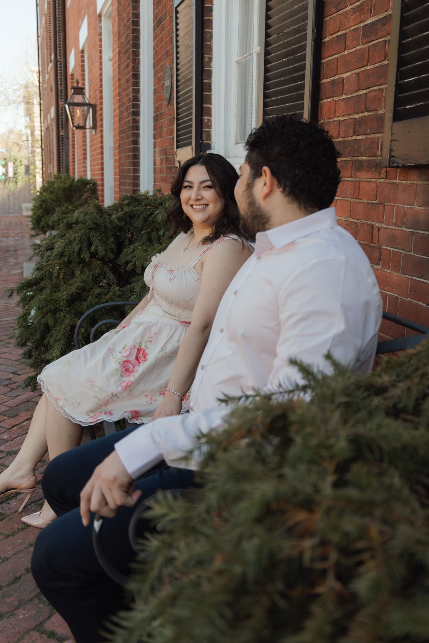 Couple sitting on brick steps outside a historic building, woman in floral dress smiling at man in white shirt.
