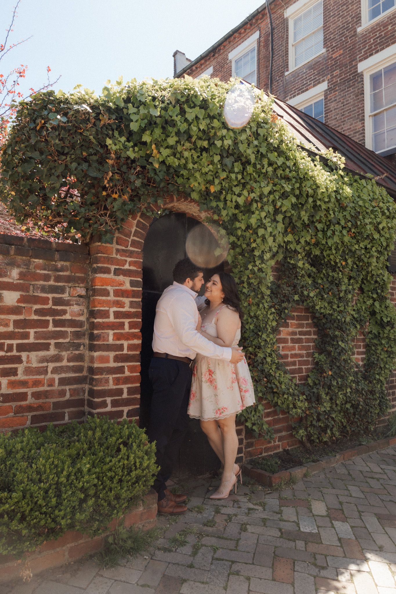 Couple sharing a romantic moment under an ivy-covered brick archway at a historic estate.