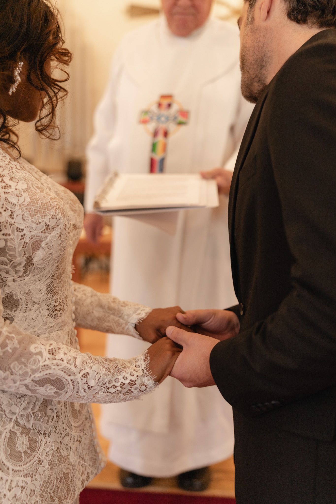 Bride and groom holding hands at altar during wedding ceremony with officiant holding book in background.