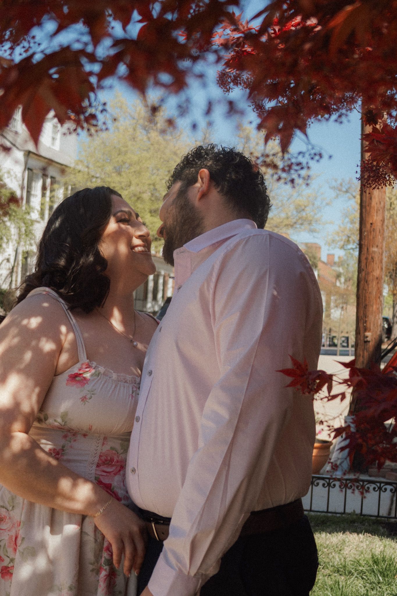 Couple sharing a romantic moment under red maple leaves on a sunny day outdoors.
