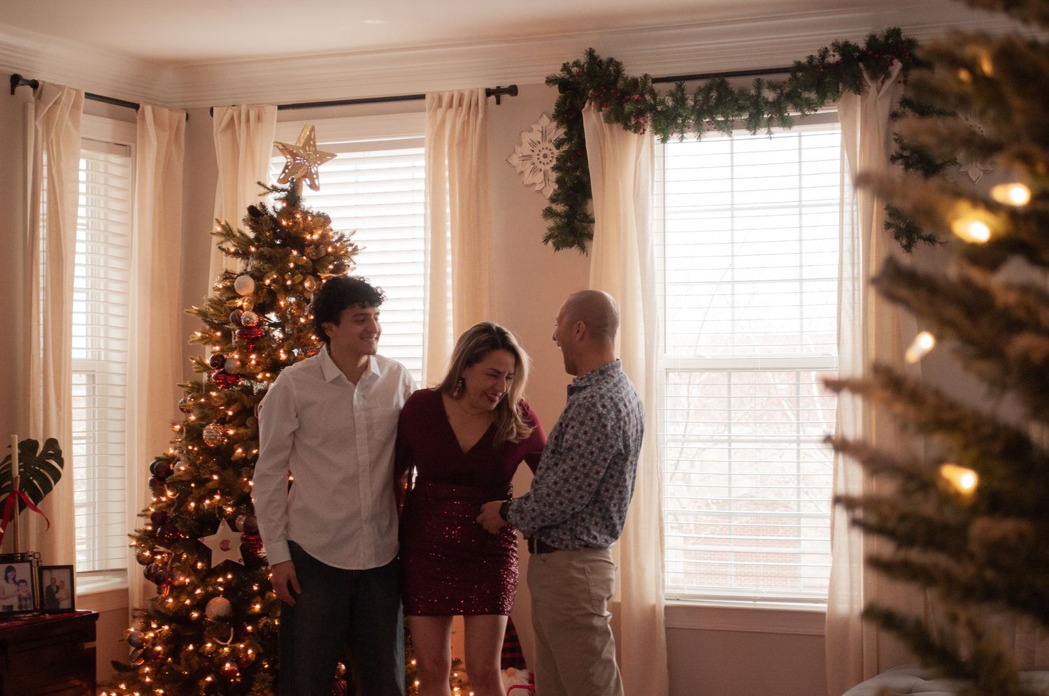 Family gathering near a decorated Christmas tree in a festive living room with garland and warm holiday lights.