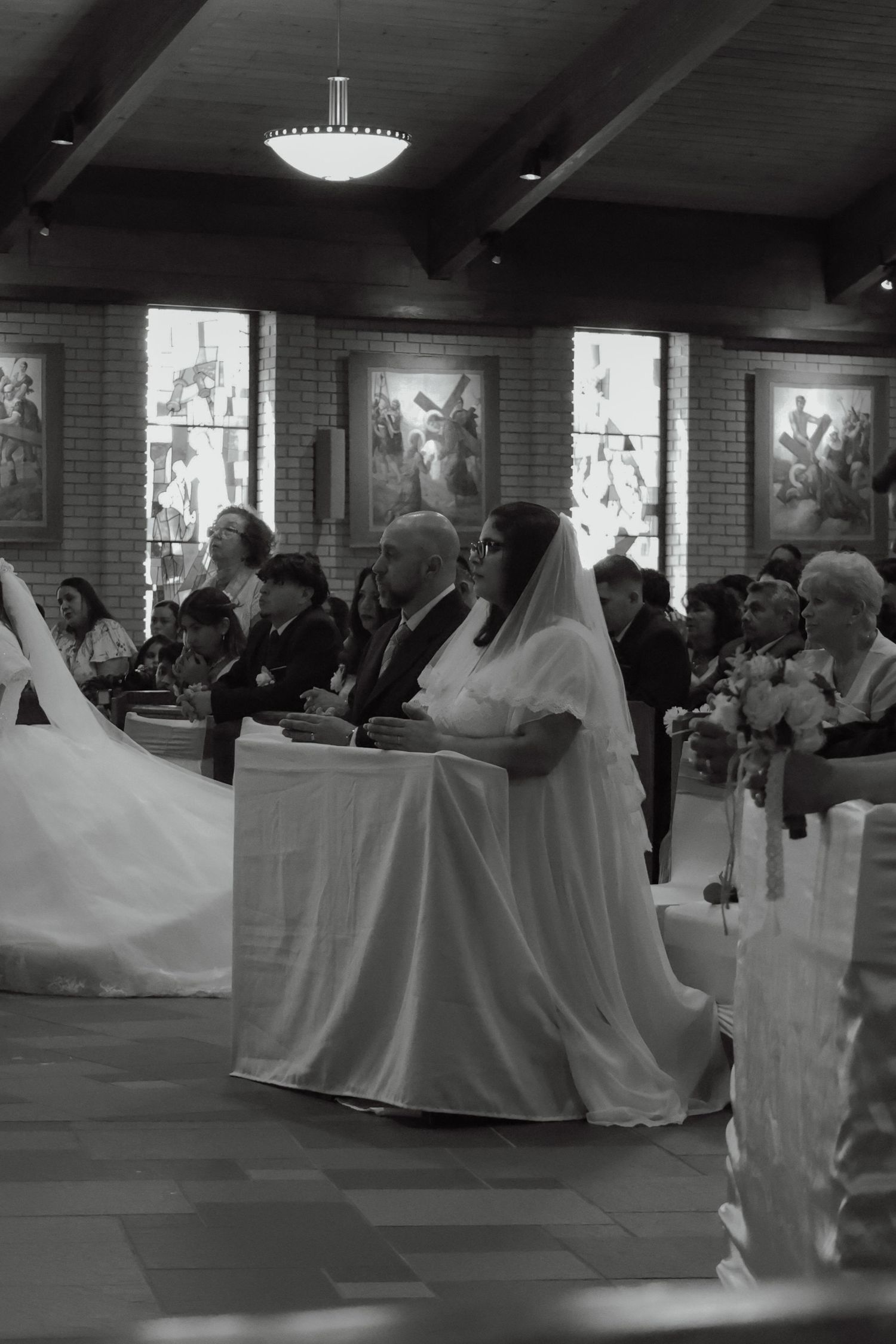 Black and white photo of a bride in veil and groom seated at church altar during wedding ceremony.