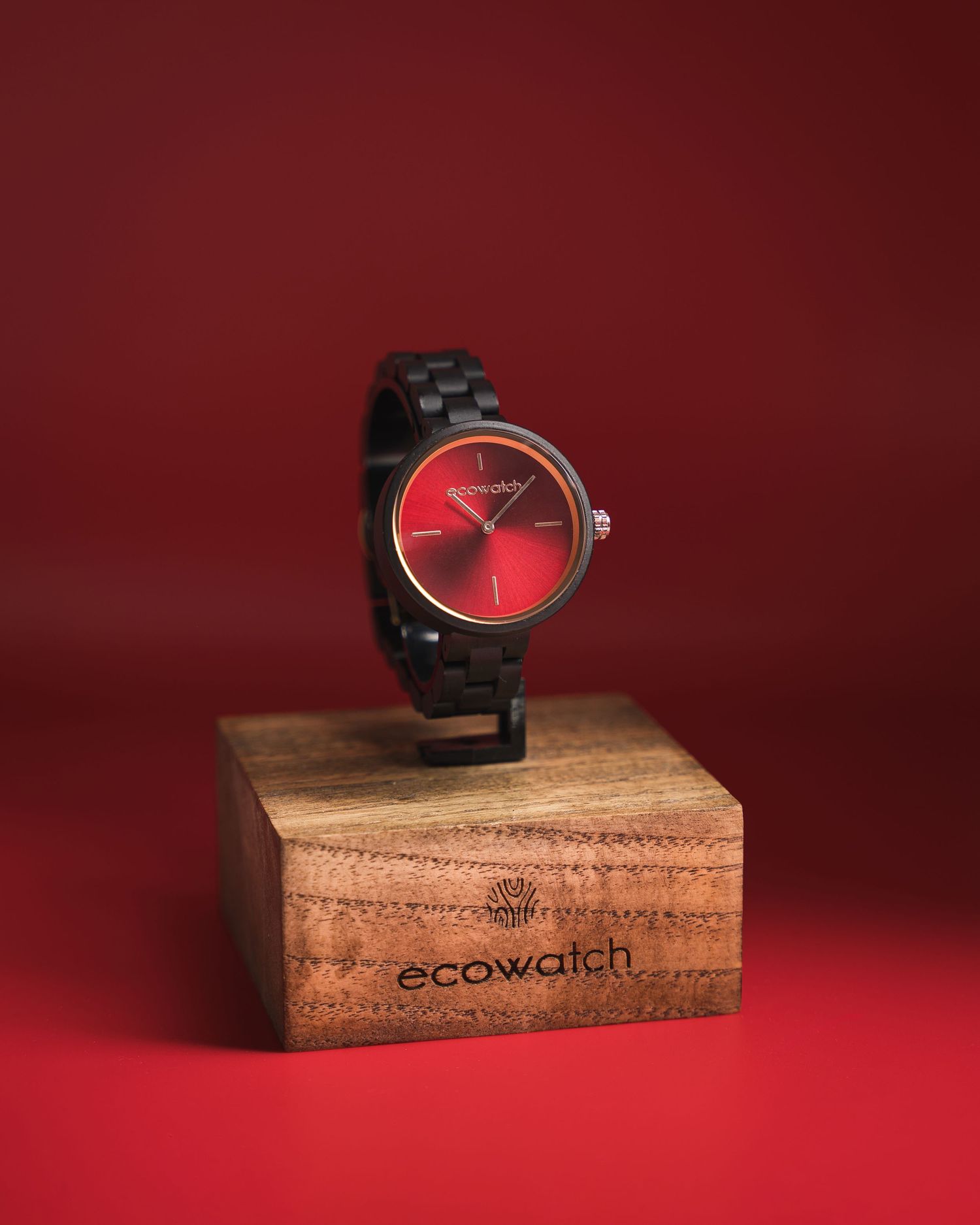 Modern wooden watch with red face displayed on rustic wooden block against dark red background.