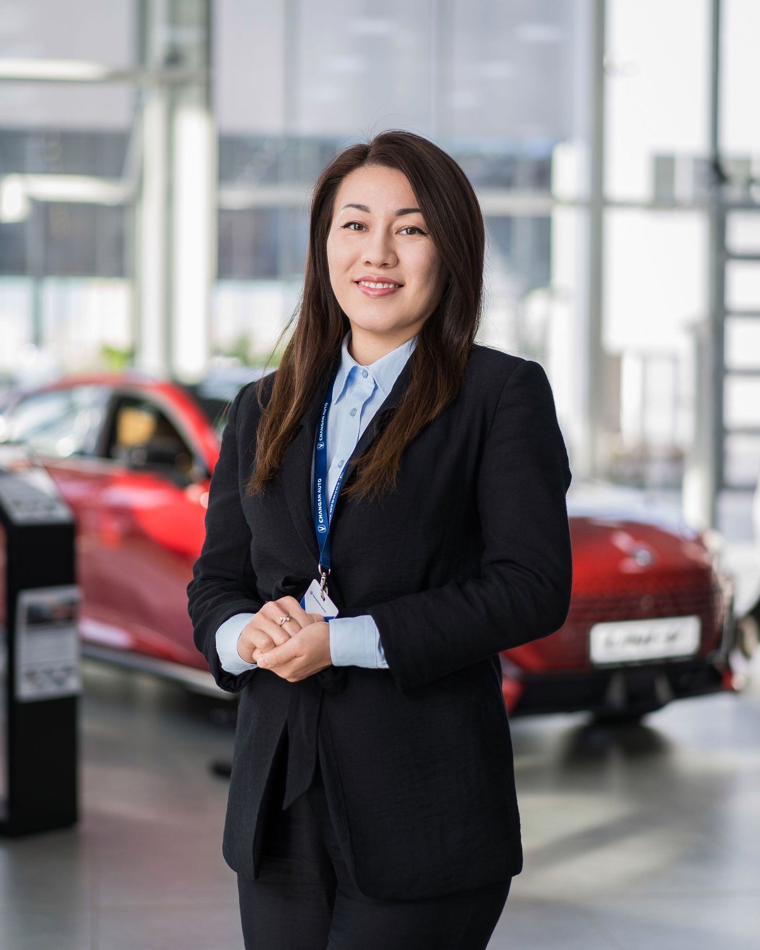 Professional in business suit standing in modern car dealership showroom.