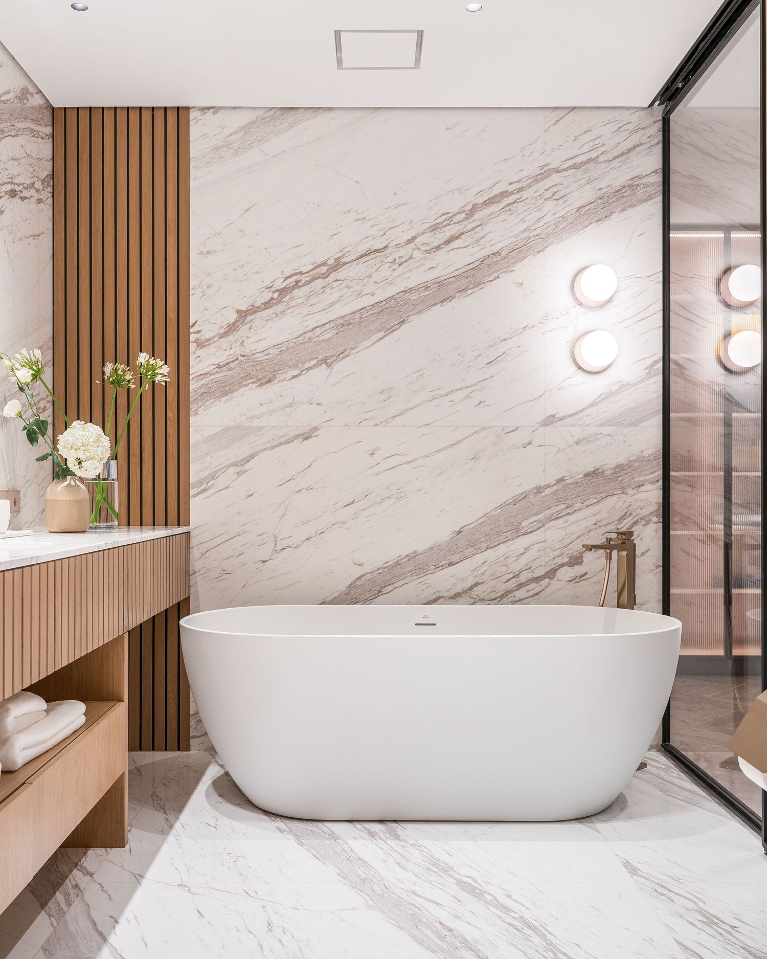 Luxurious bathroom with freestanding white bathtub and marble walls featuring wood accent panels.