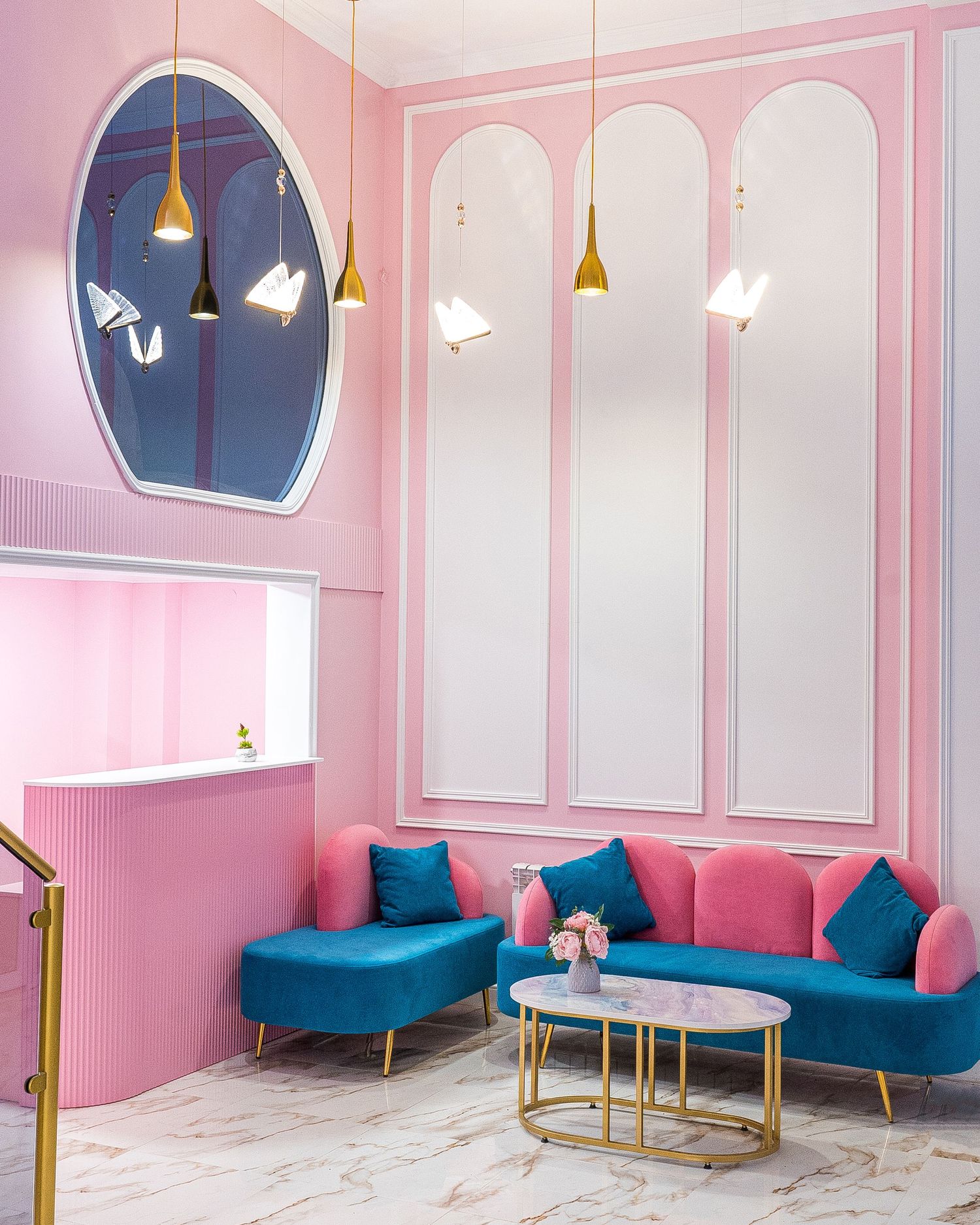Pink and blue lounge area with velvet sofas, gold accents, and arched wall details.