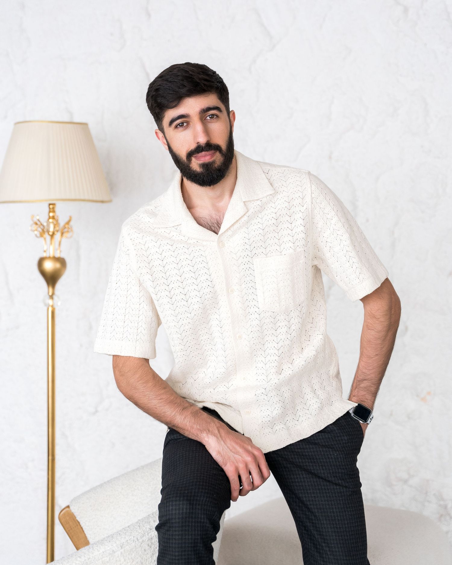 Person wearing white knit sweater and dark pants posing near decorative floor lamp.