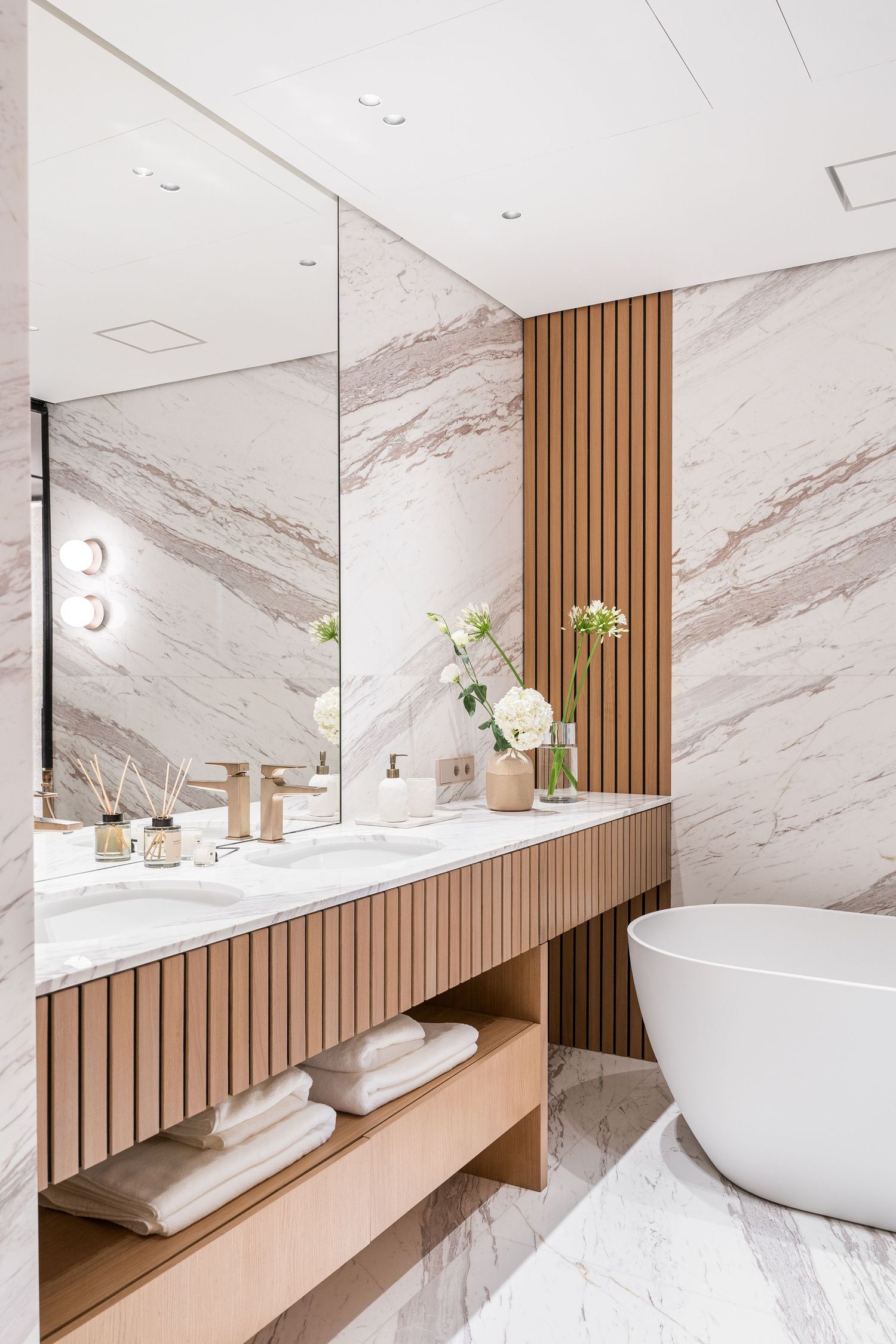 Spa-like bathroom featuring white marble walls, wooden panels, and modern freestanding tub.