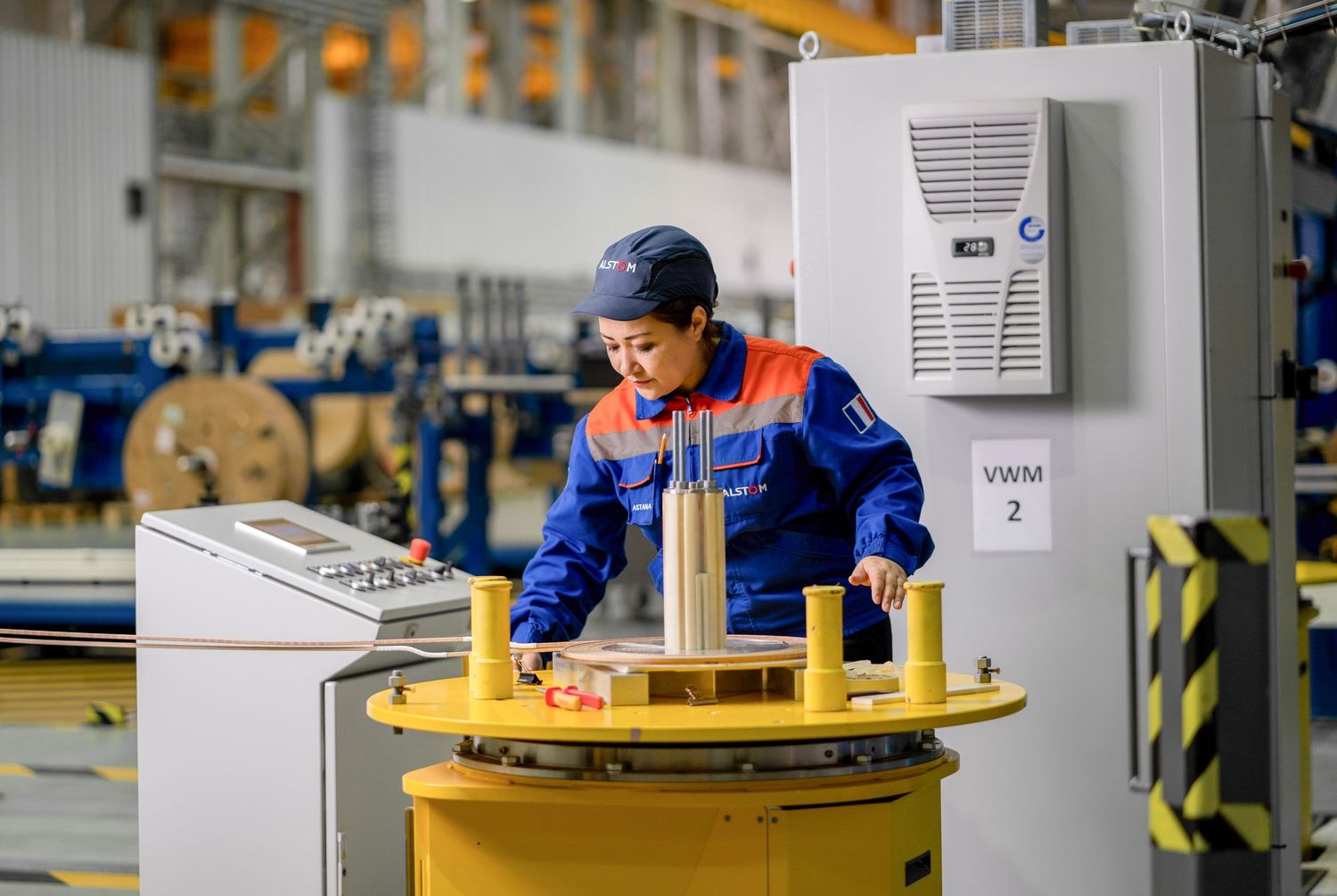 Worker in blue uniform operating industrial equipment at control station in manufacturing facility.