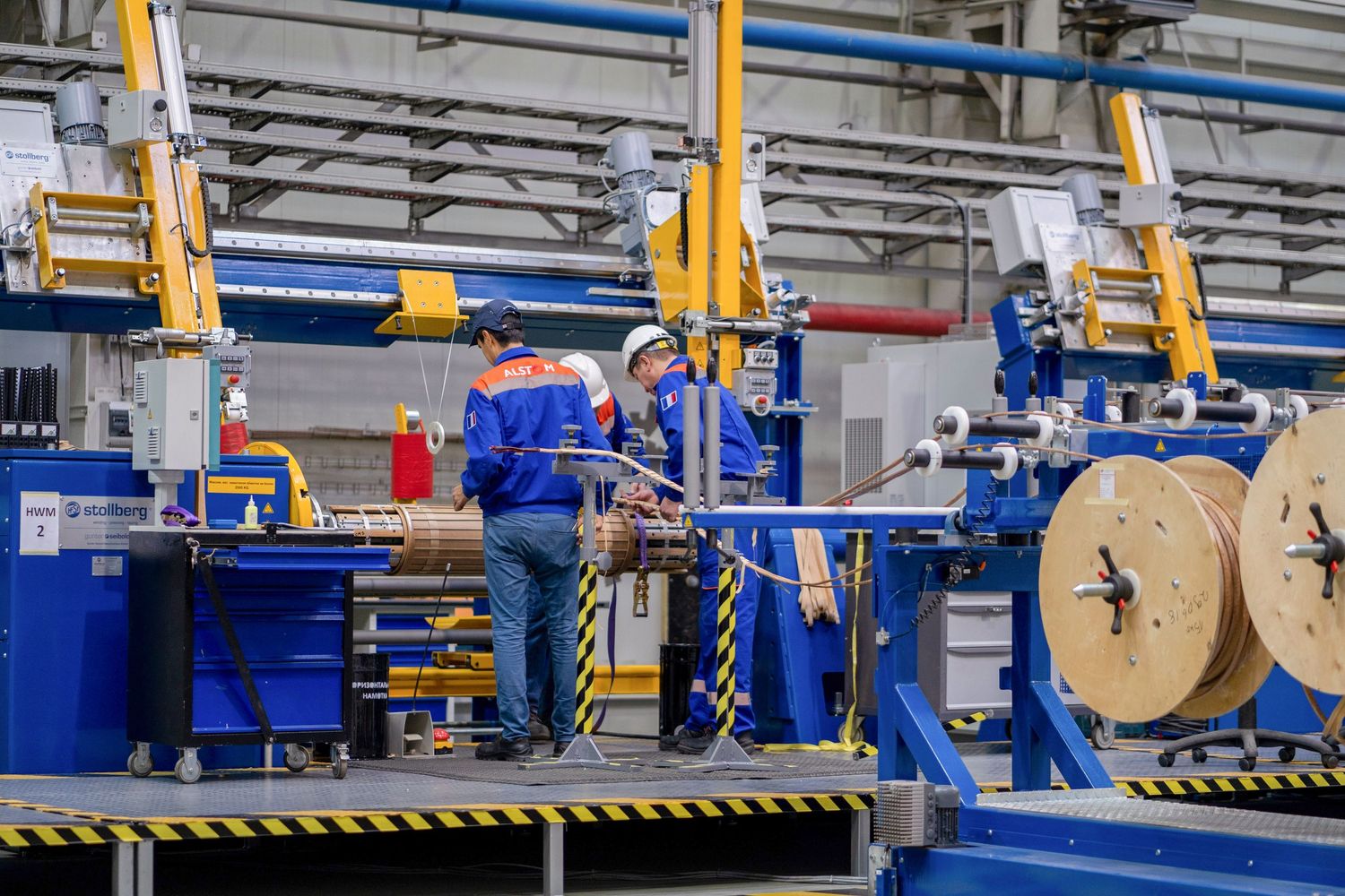 Manufacturing facility with workers operating blue machinery and equipment on production line.