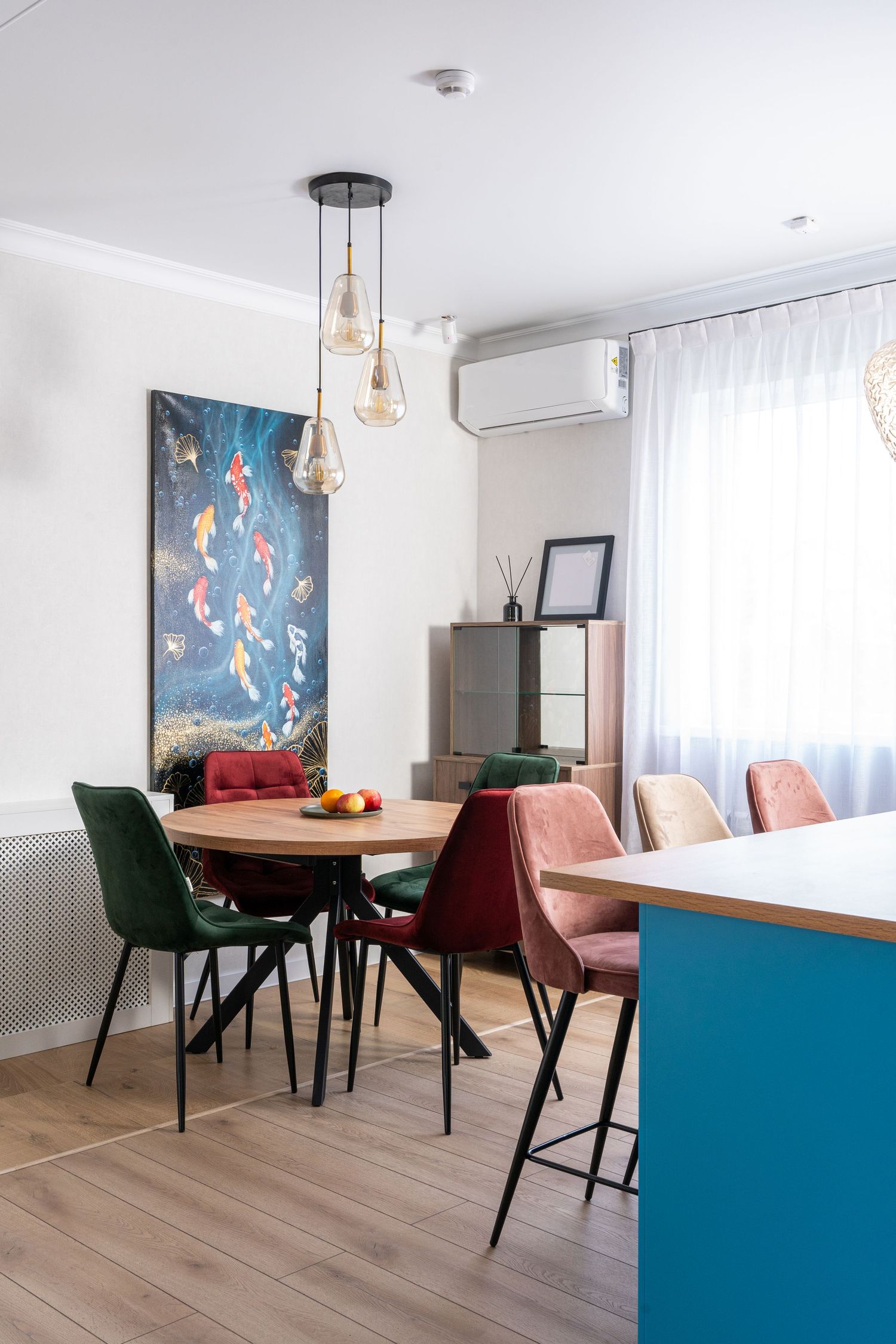 Modern dining area with blue accent wall, green velvet chairs, and pendant lighting in an open concept space.