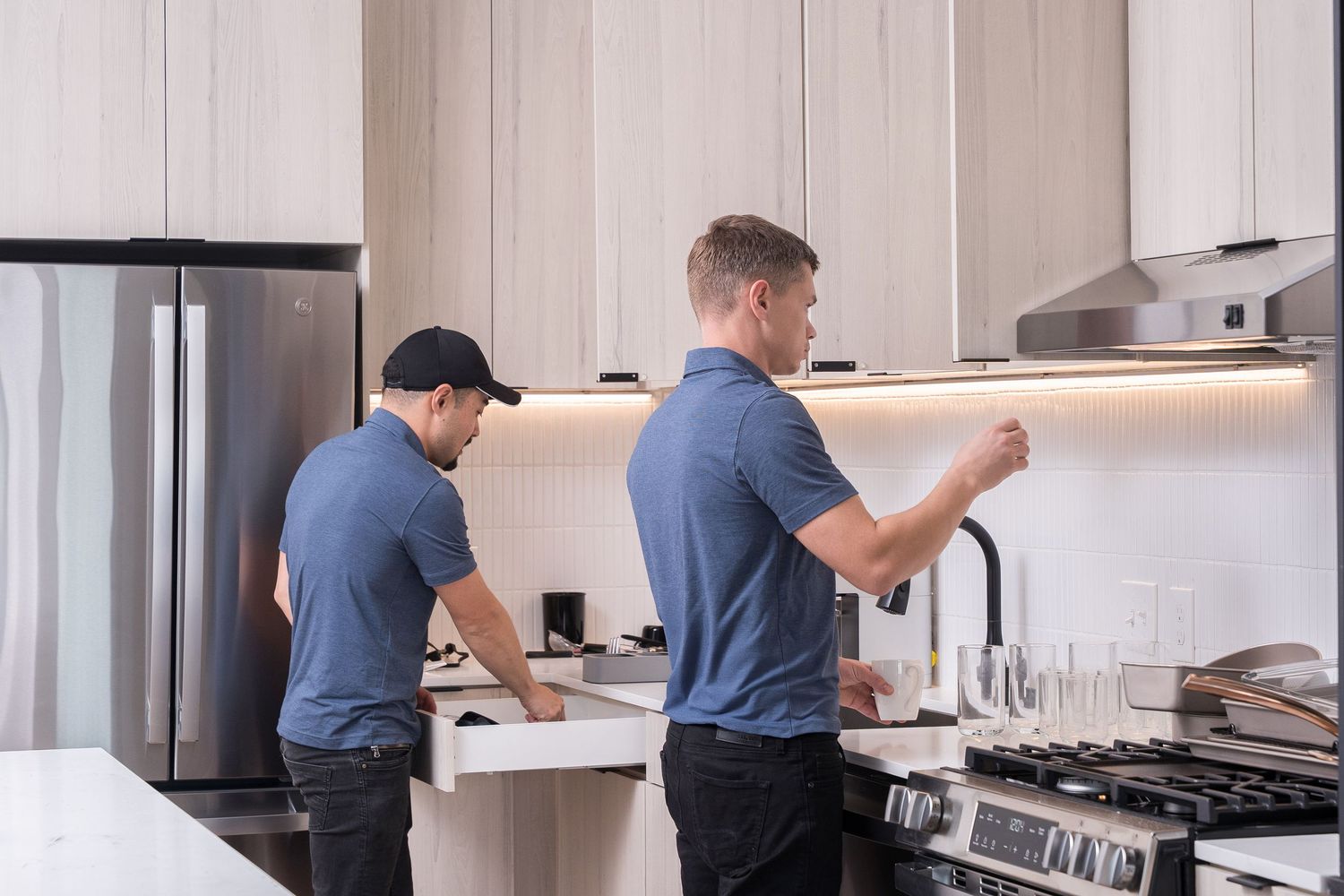 Professional technicians working on kitchen appliance installation in modern white kitchen.