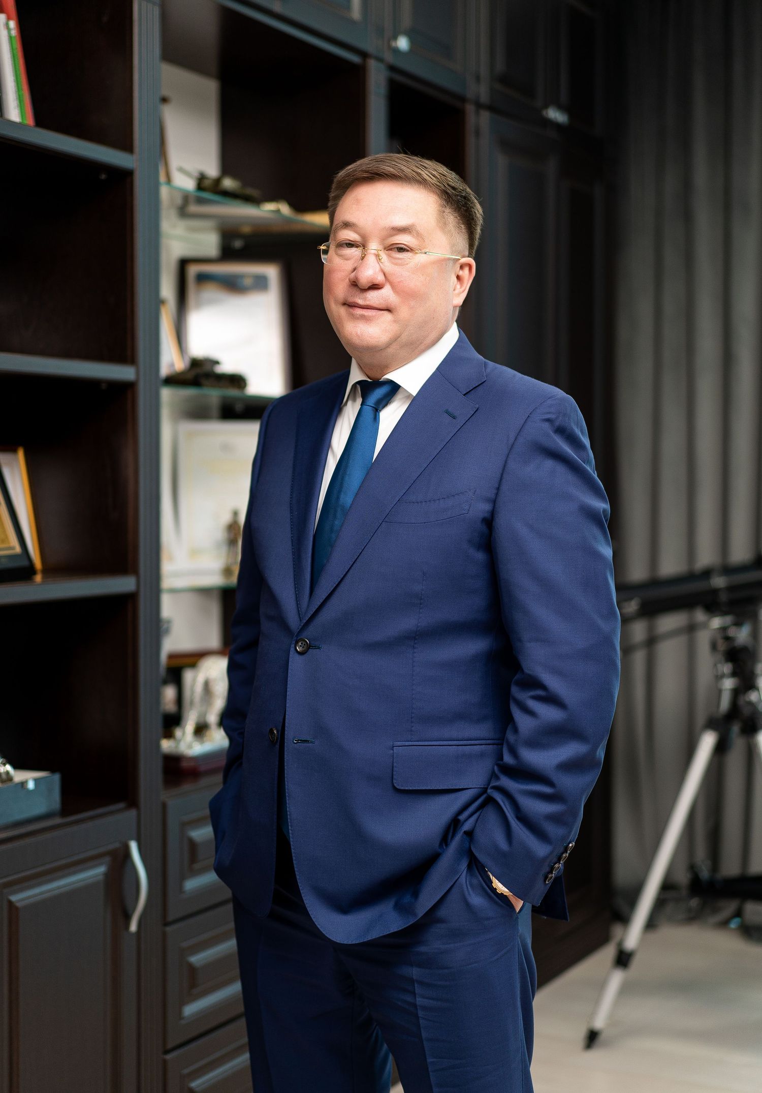 Professional office photoshoot of businessman in navy suit against dark interior.