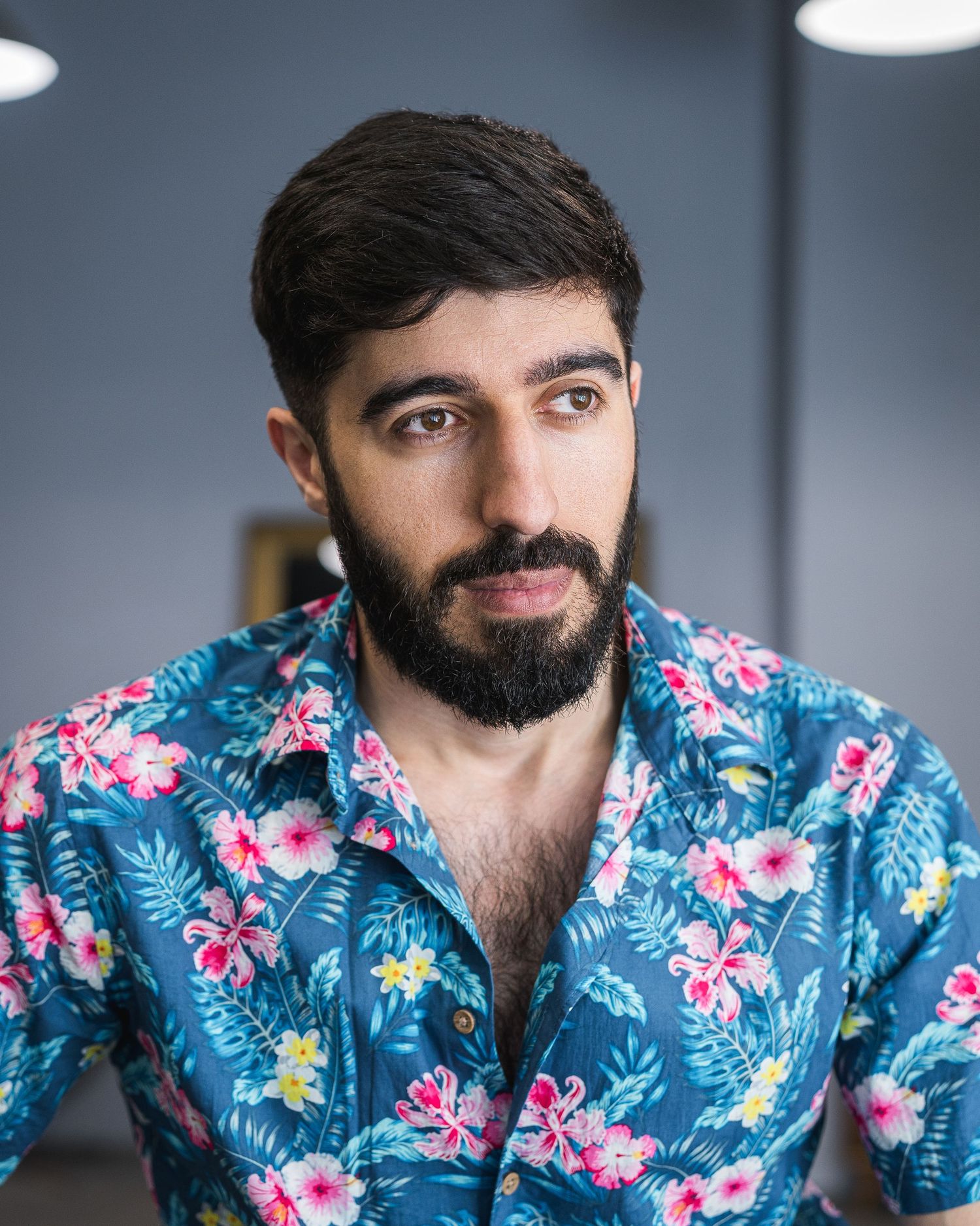 Person wearing tropical floral print shirt smiling against gray background.