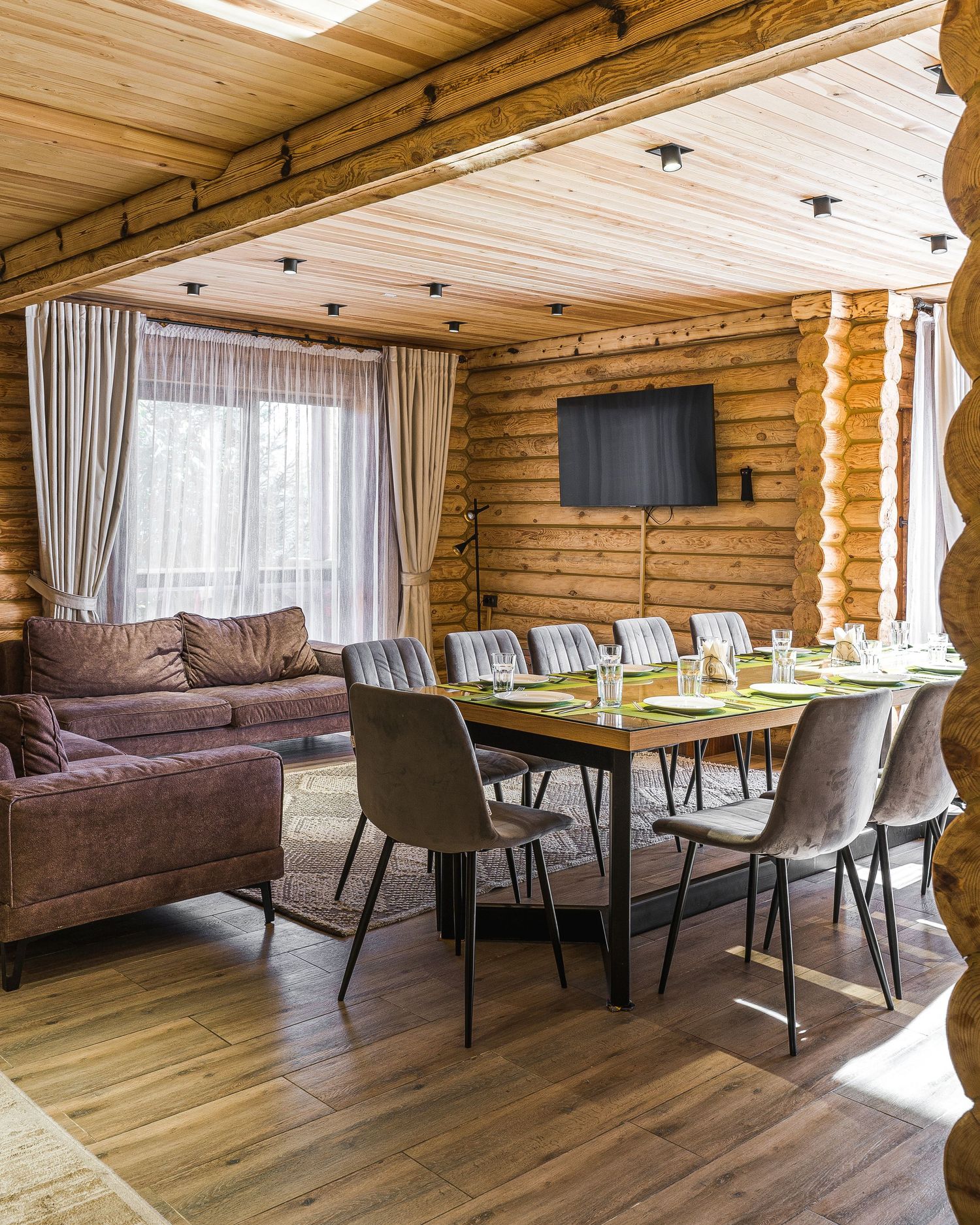 Rustic log cabin interior with wooden walls, modern furniture, and large windows creating a cozy dining space.