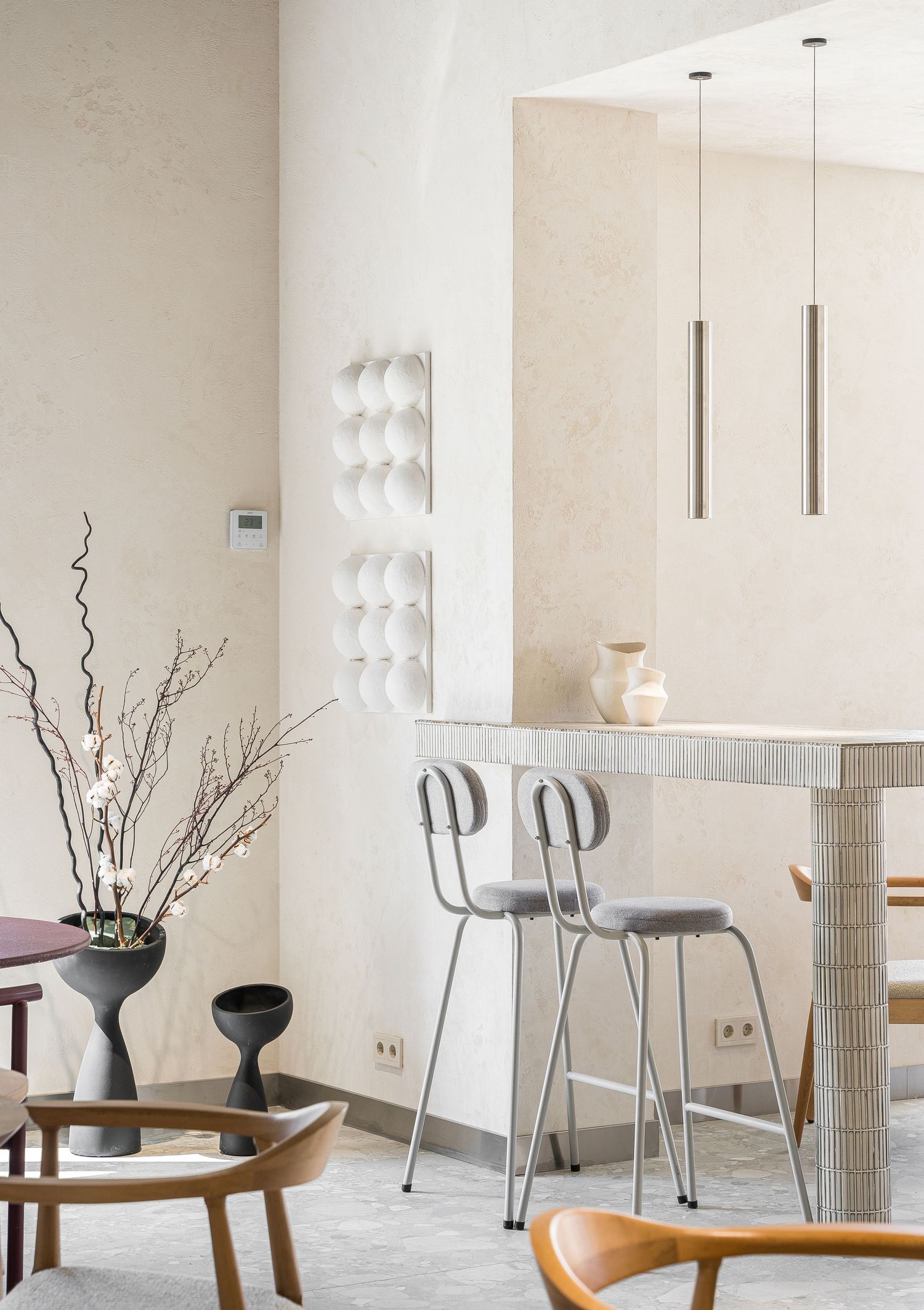 Modern minimalist dining room with wooden tables, metal chairs, and white vases with decorative branches.