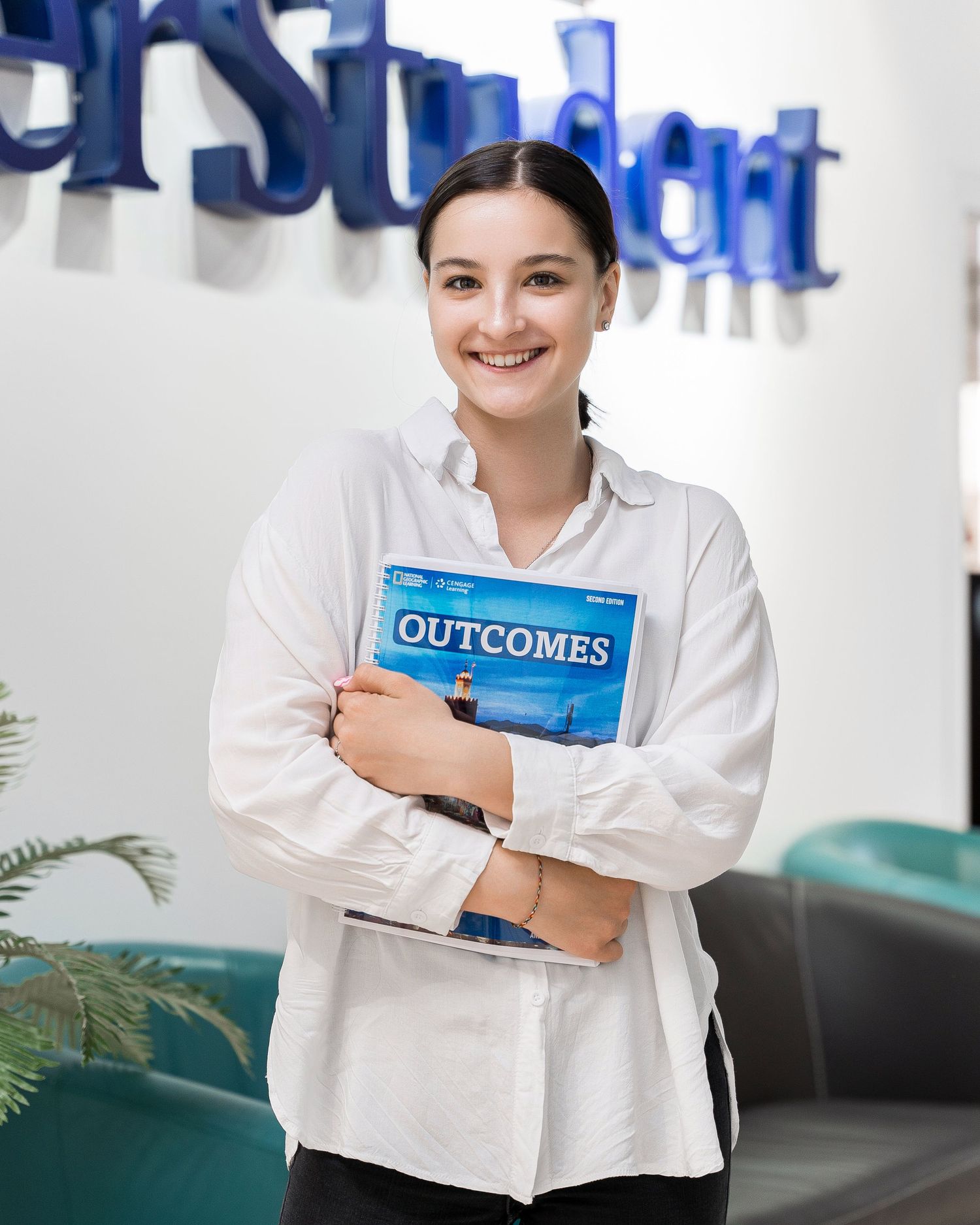Language school staff member holding blue textbook in modern office setting.