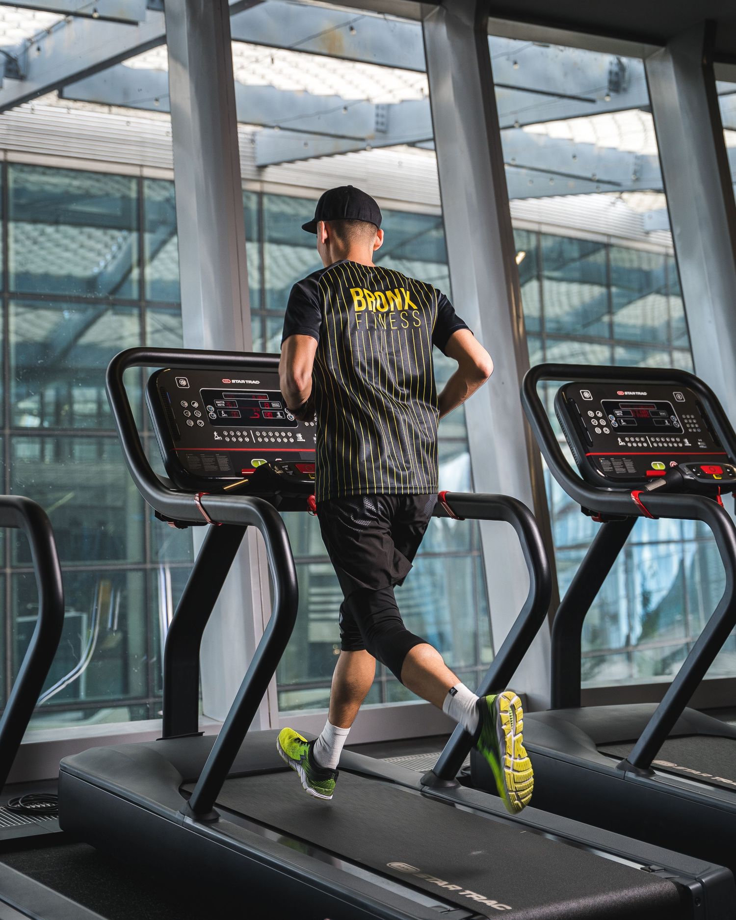 Person running on treadmill in modern fitness center with glass windows.