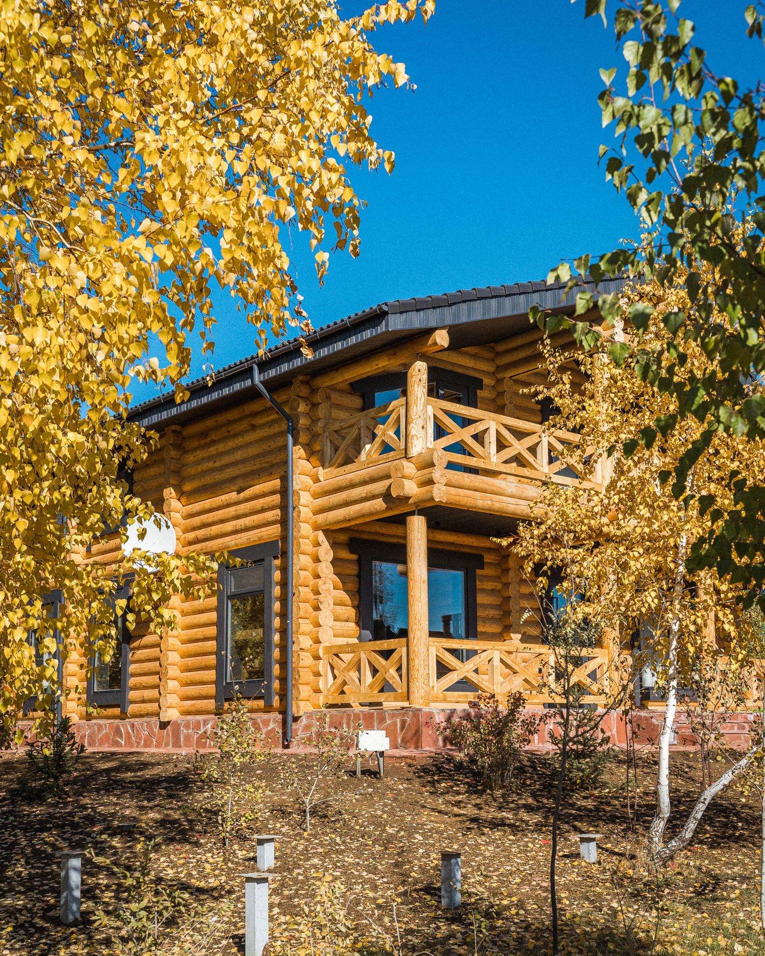 Log cabin exterior surrounded by golden autumn trees against bright blue sky.