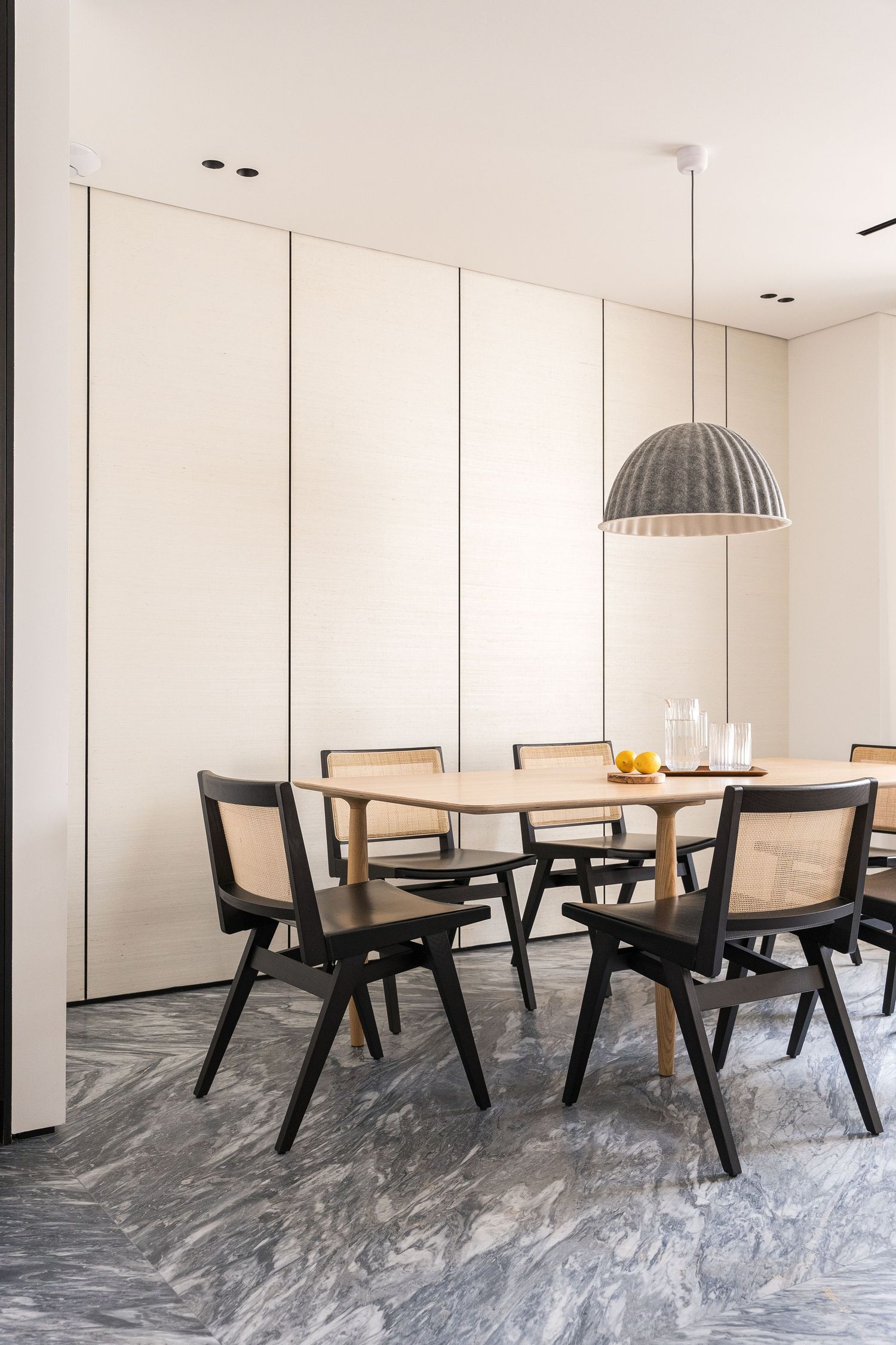 Minimalist dining area with black wooden chairs and pendant lighting on dramatic marble flooring.