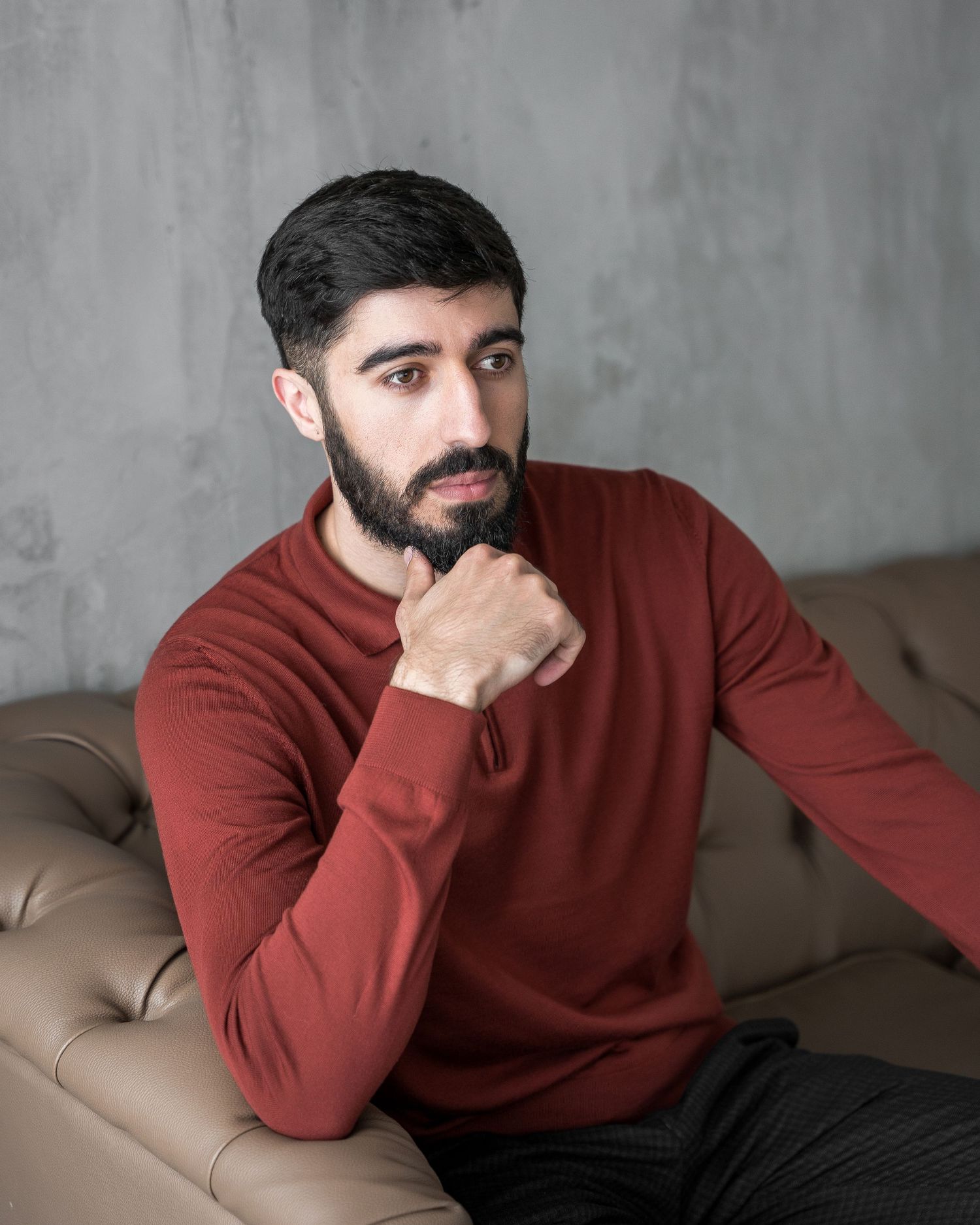 Person in burgundy sweater relaxing on beige couch against gray wall.