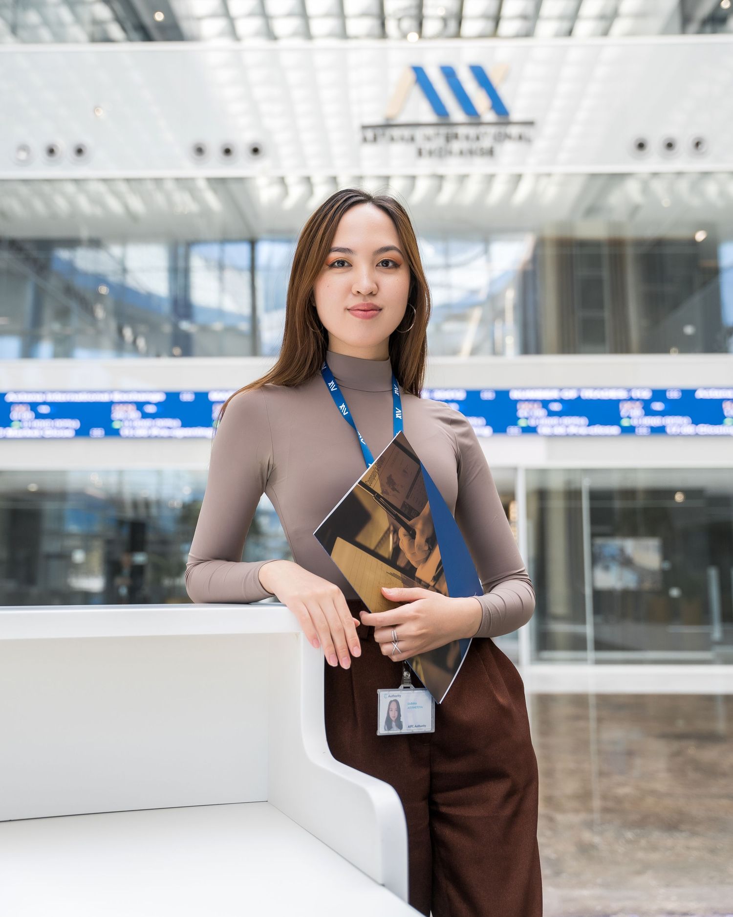 Professional woman in brown outfit holding documents in modern airport terminal.