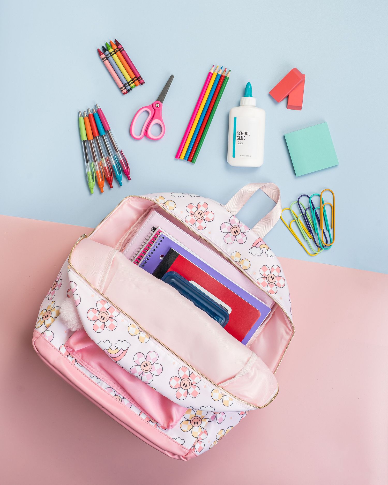 Pink pencil case with school supplies scattered on pastel blue and pink background.