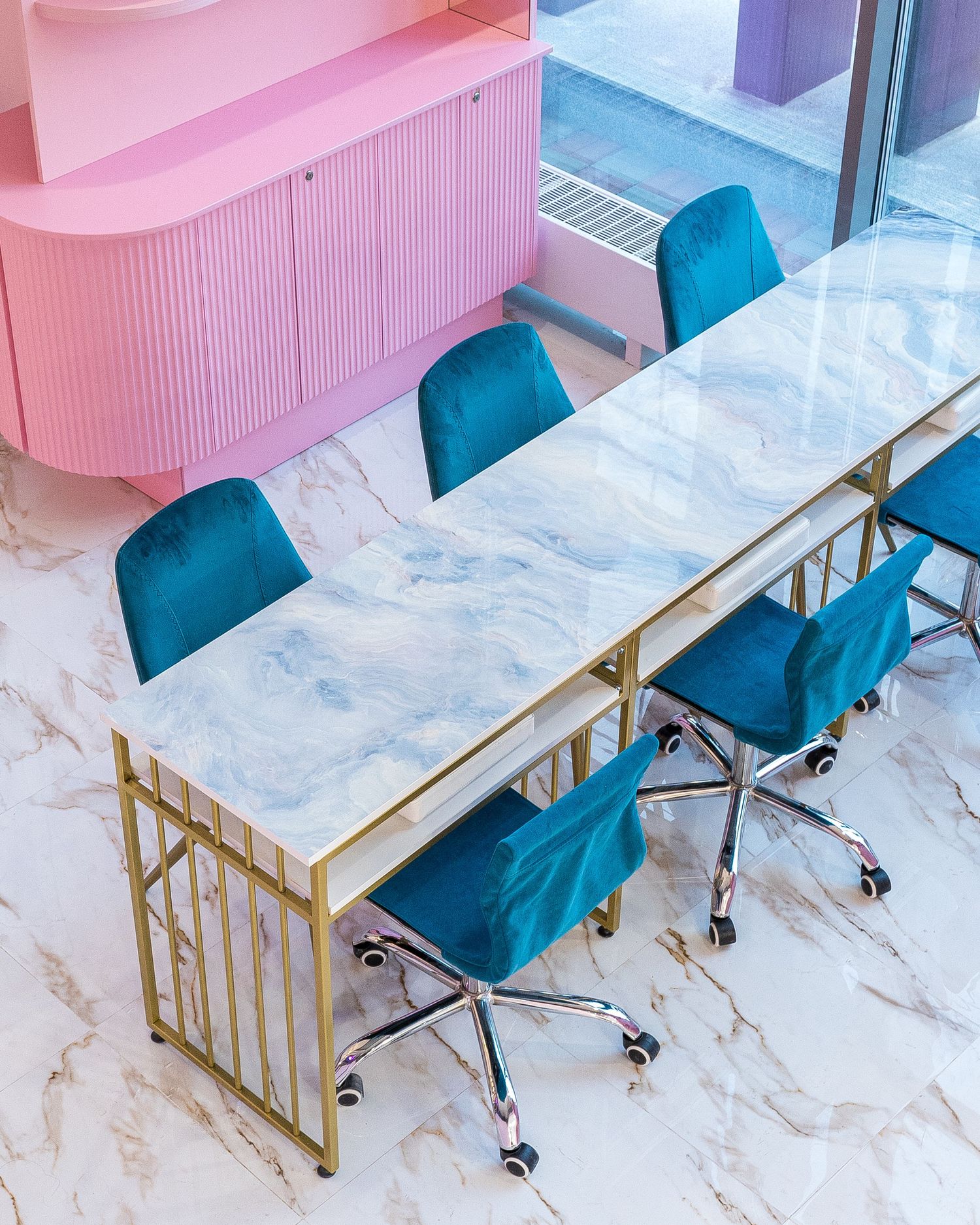 Sleek dining area with marble tables, teal chairs, and gold accents in a contemporary setting.