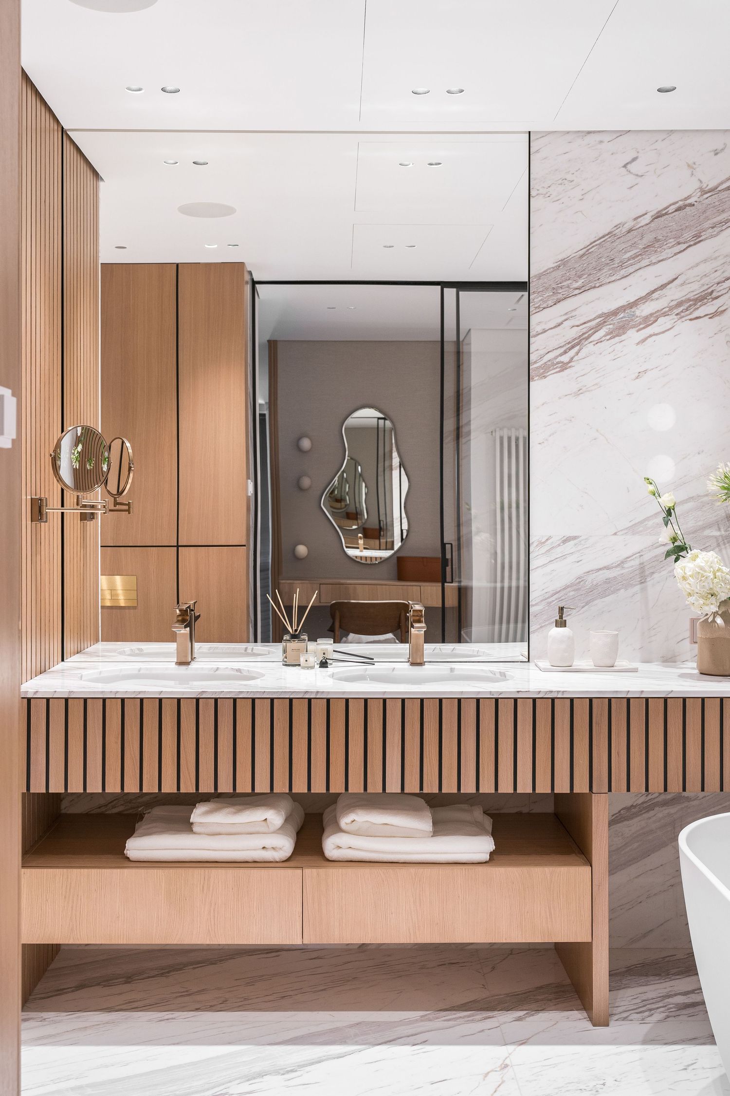 Modern bathroom vanity with wooden slat design, mirrors, and marble wall finishes.