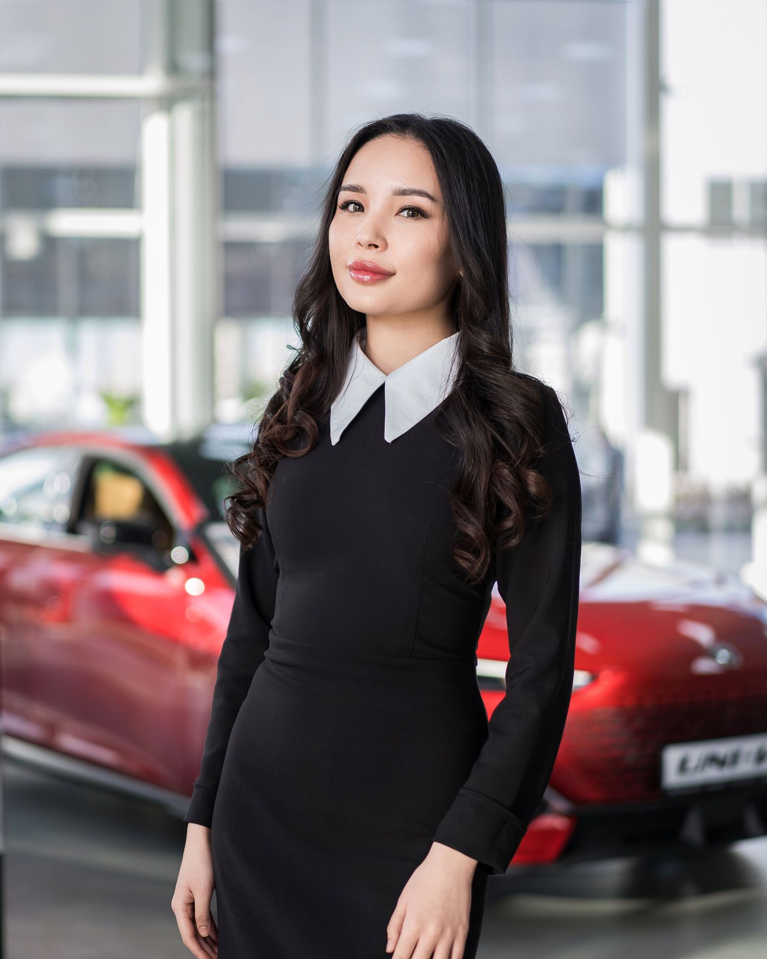 Professional in black dress with white collar standing in car dealership showroom.