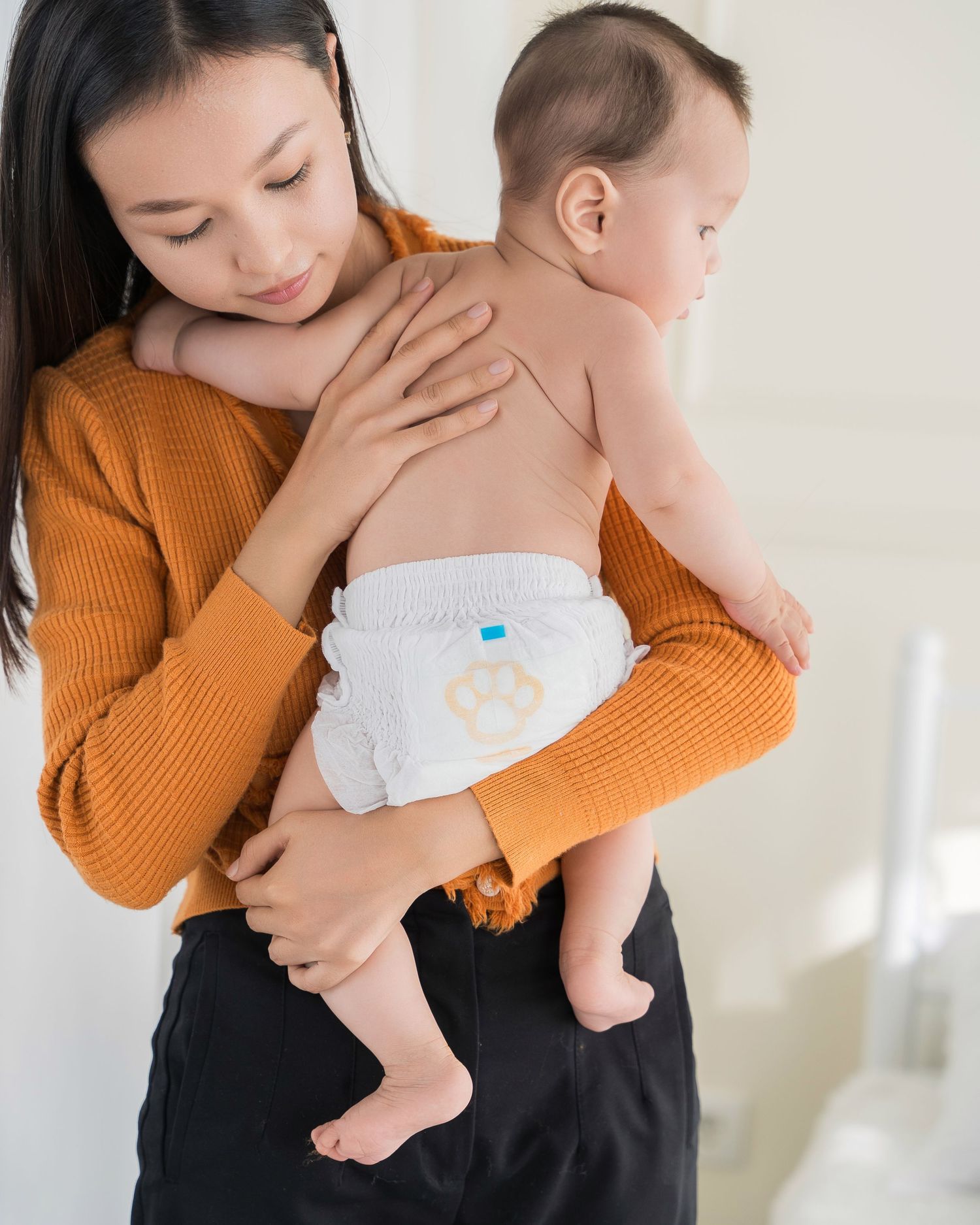 Parent in orange sweater holding and comforting baby in white diaper.