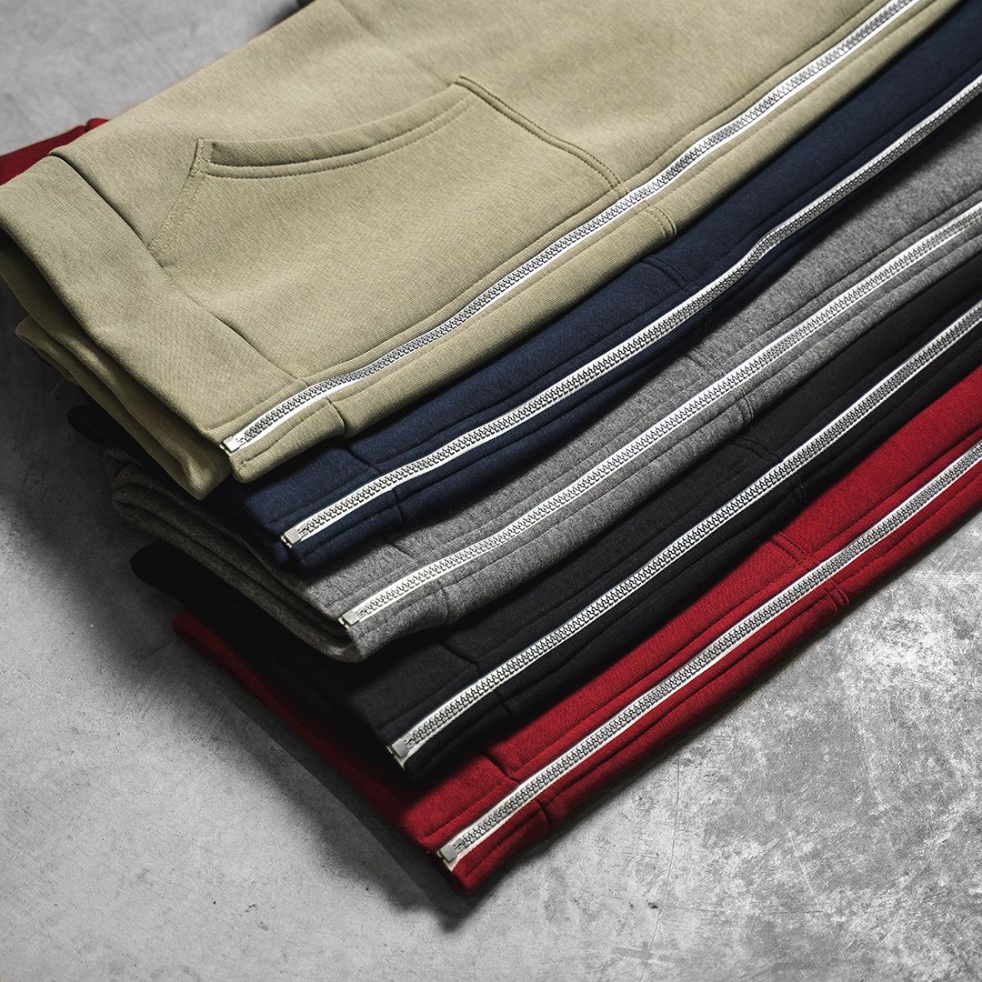 Stack of folded sweatpants in neutral colors including beige, navy, grey and red.
