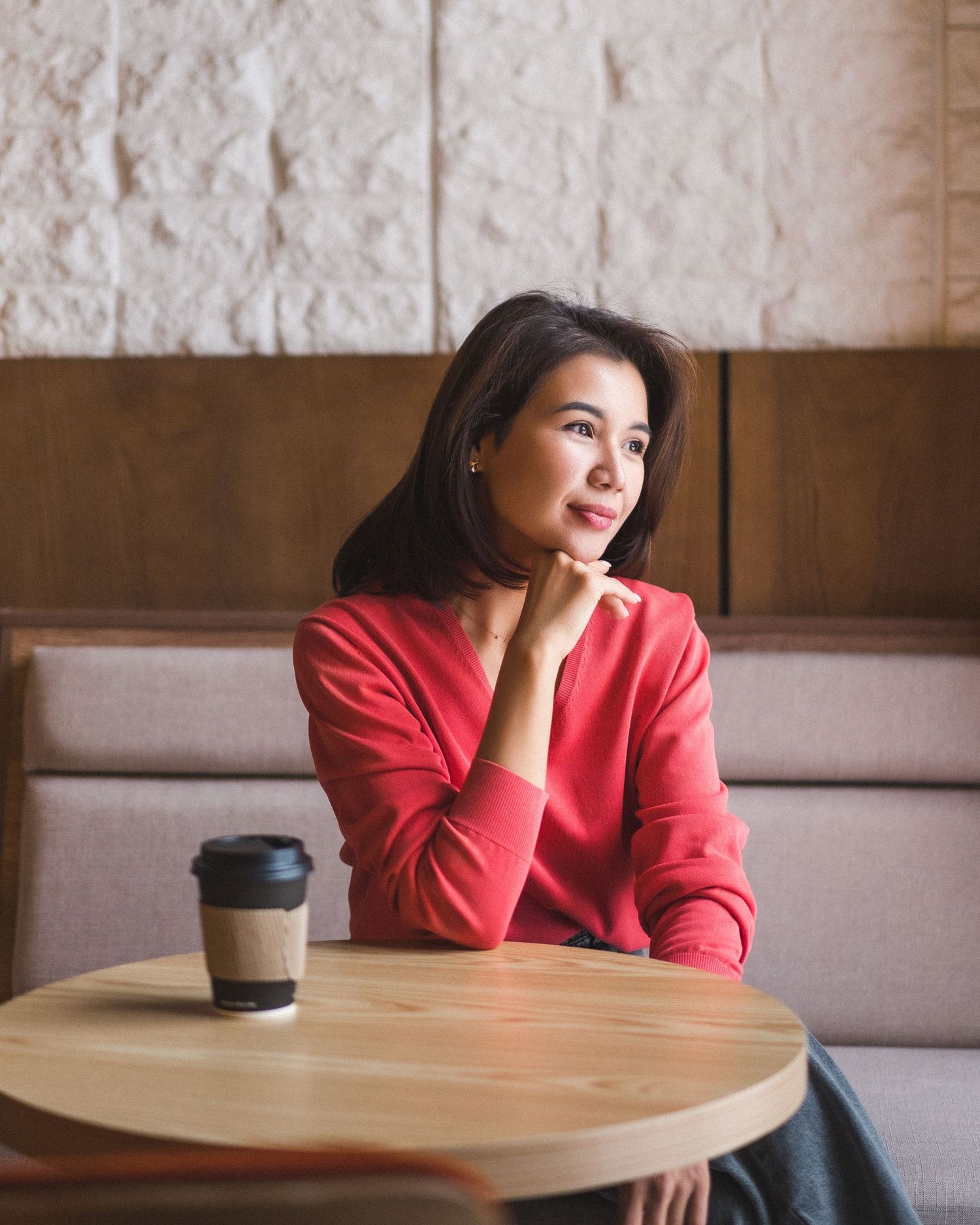 Person wearing red blazer sitting at cafe table with coffee cup.