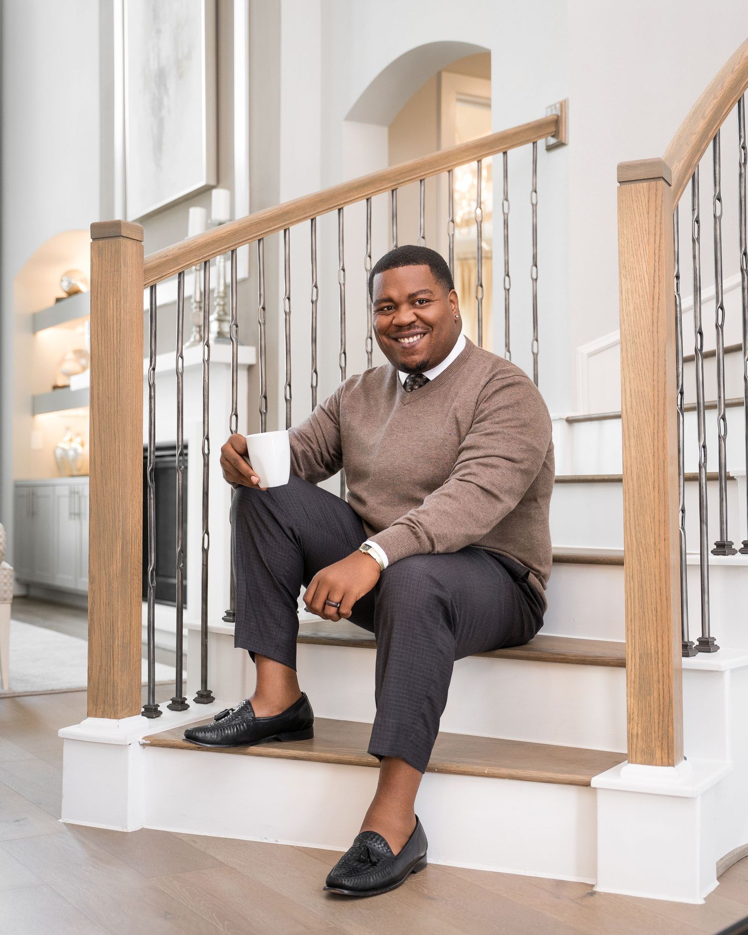 Person in brown sweater sitting casually on white stairs with wooden railings.