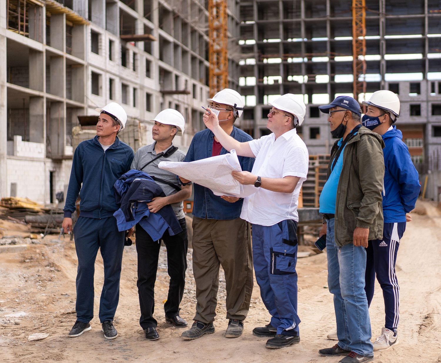 Group of construction professionals examining building plans at an unfinished development site.