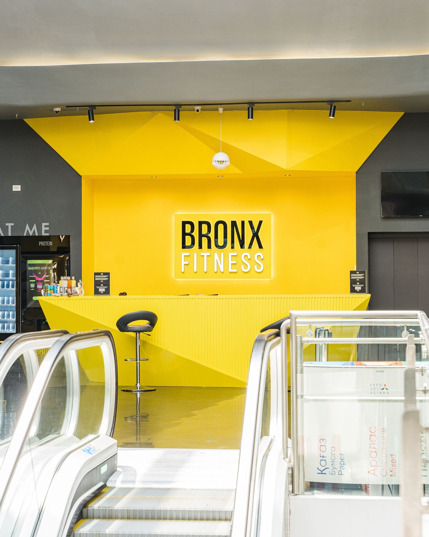 Modern fitness center entrance with bright yellow walls displaying 'BRONX FITNESS' branding.