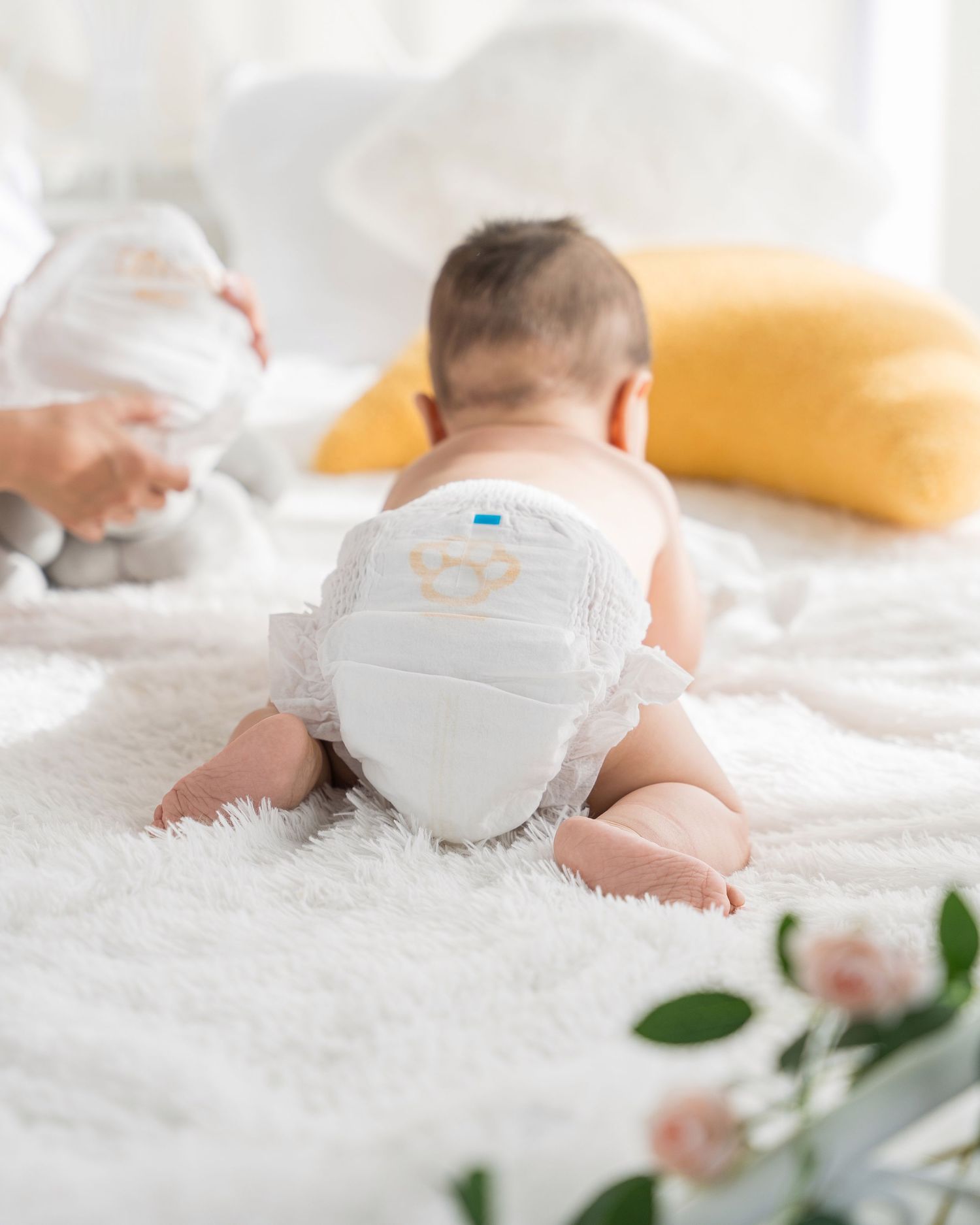 Baby lying on soft white blanket wearing a diaper with delicate flowers in the scene.