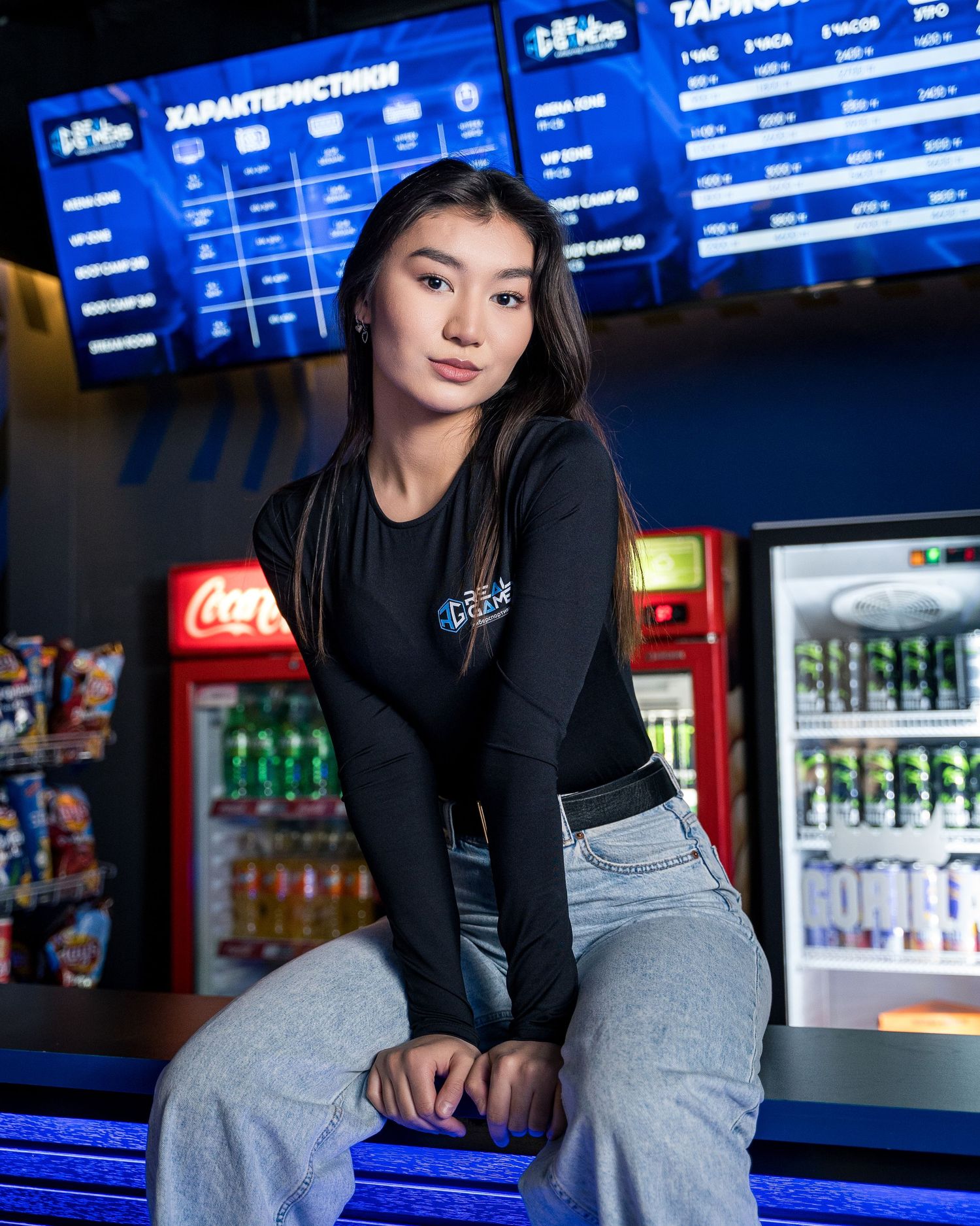 Person in casual attire sitting at a gaming center with blue digital displays in the background.