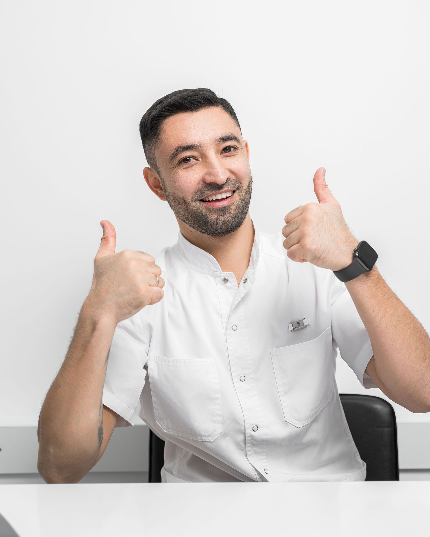 Healthcare professional in white uniform giving thumbs up while sitting at desk.