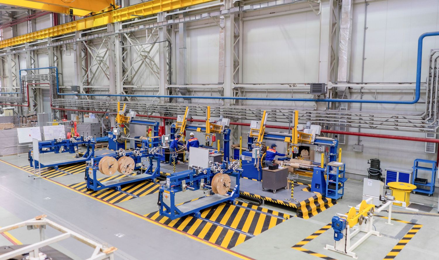 Modern factory floor with blue industrial equipment and yellow hazard markings arranged in rows.