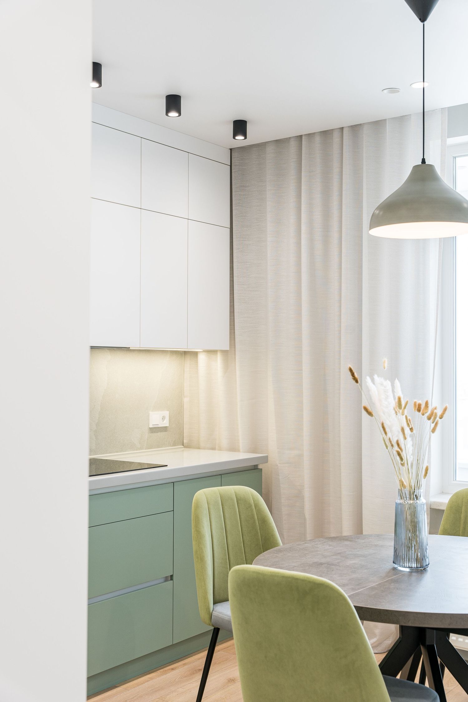 Modern kitchen space with mint green cabinets, white walls, and plush velvet dining chairs.