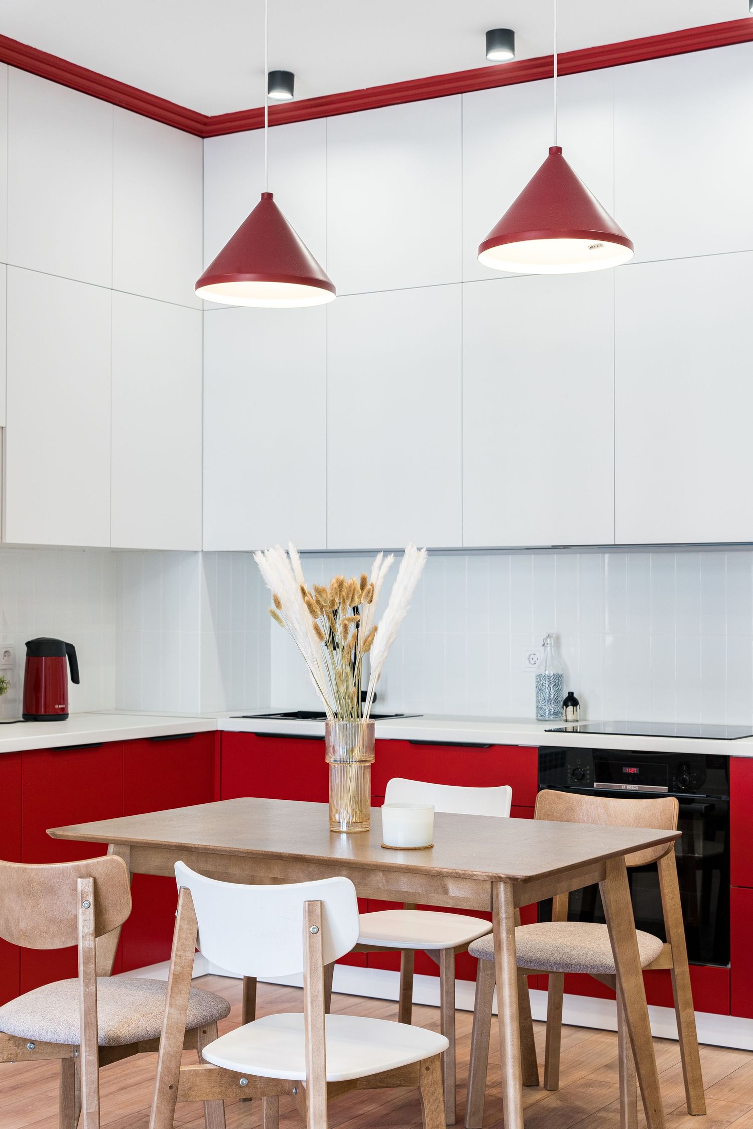 Contemporary kitchen featuring red and white cabinets with cone-shaped pendant lights above dining area.