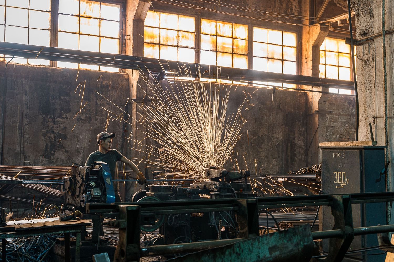 Sunlight streams through windows in an industrial manufacturing facility with machinery.