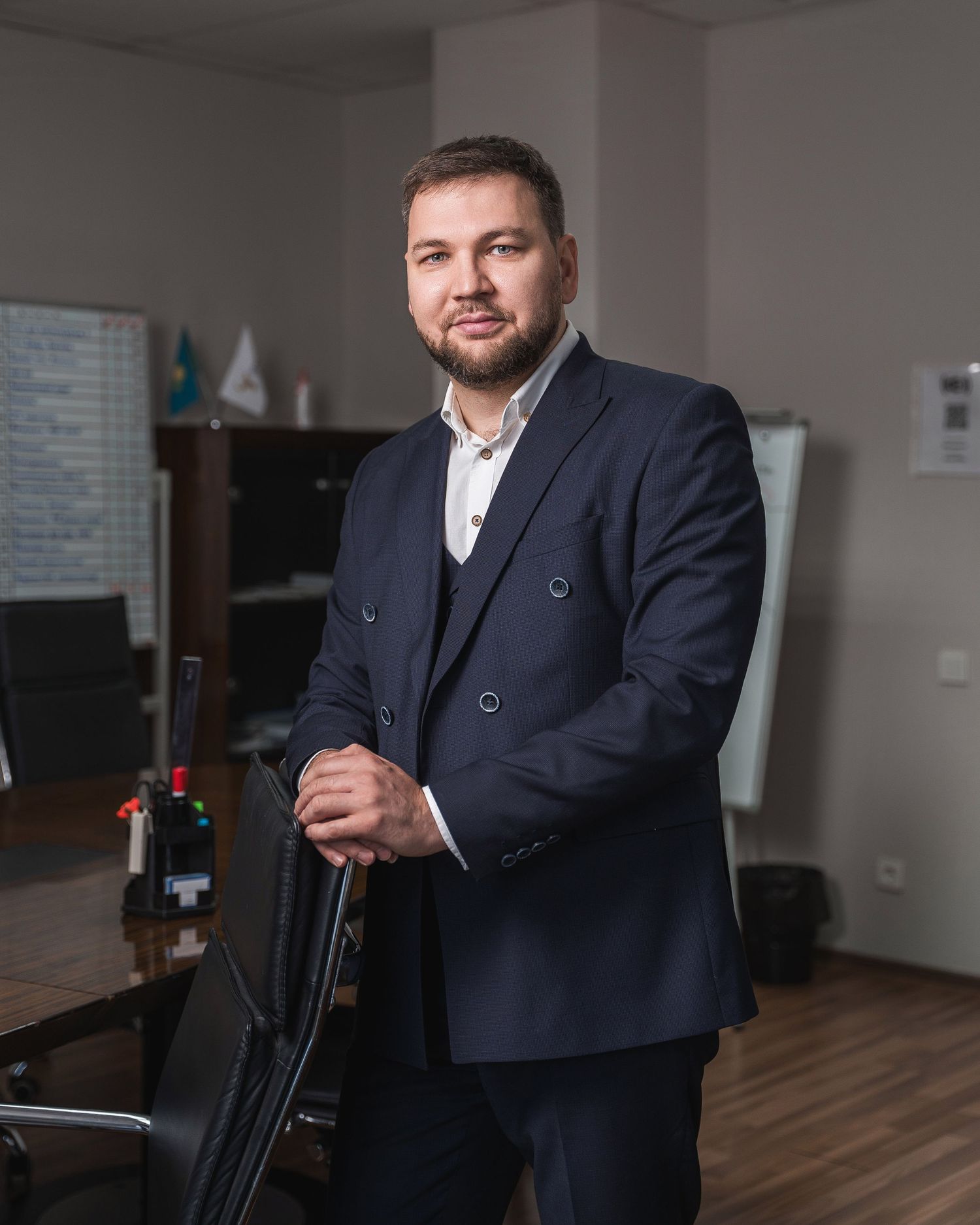 Business professional in dark suit sitting in modern office chair during corporate photoshoot.