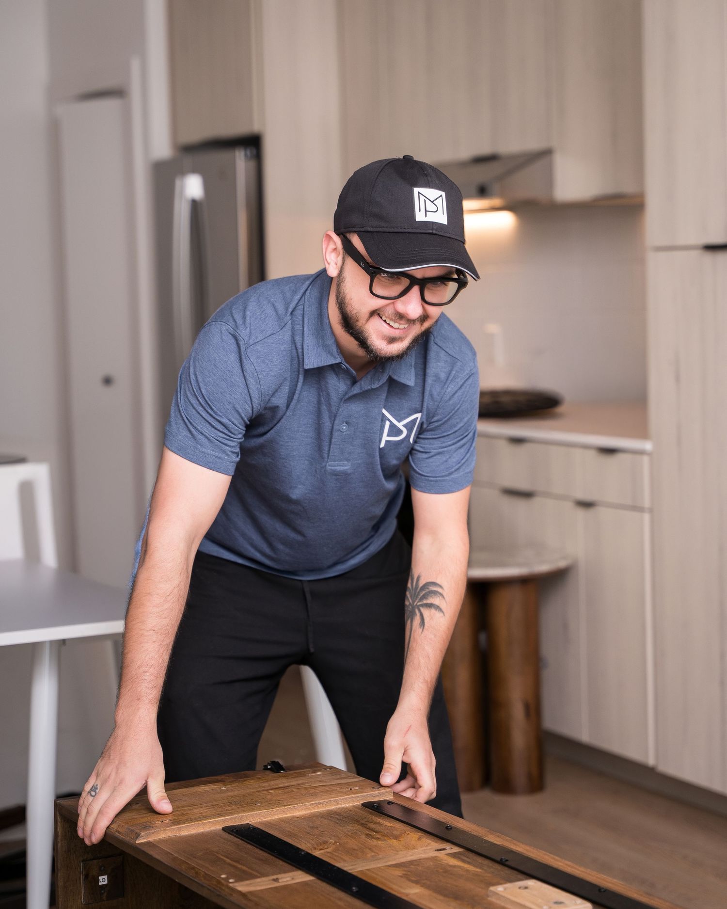 Person in blue polo shirt and black pants working with wooden furniture pieces.