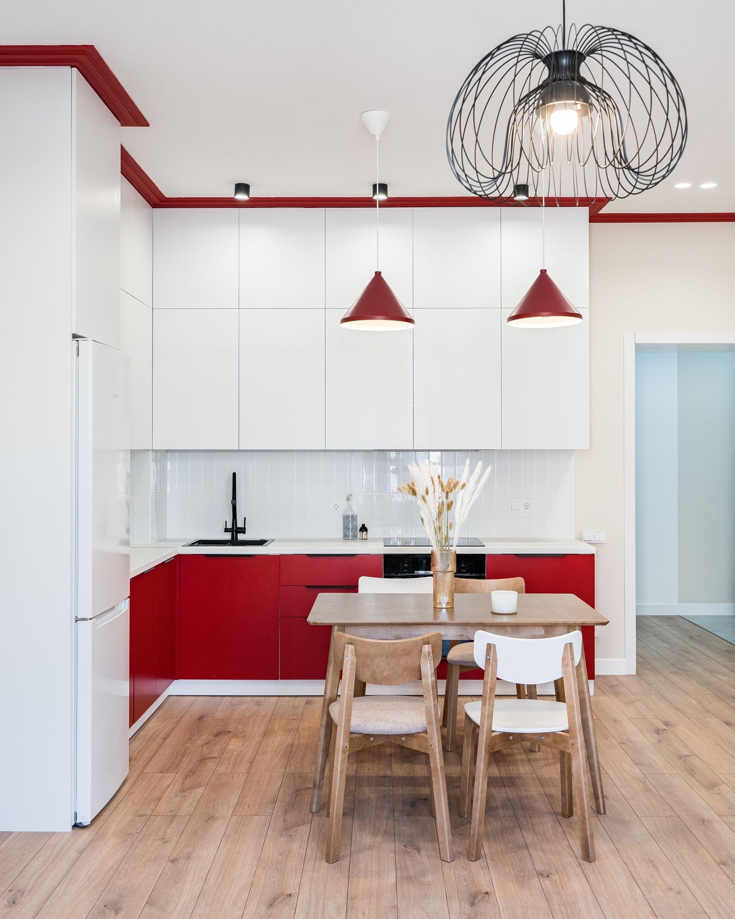 Modern white and red kitchen with pendant lights and wooden dining table.