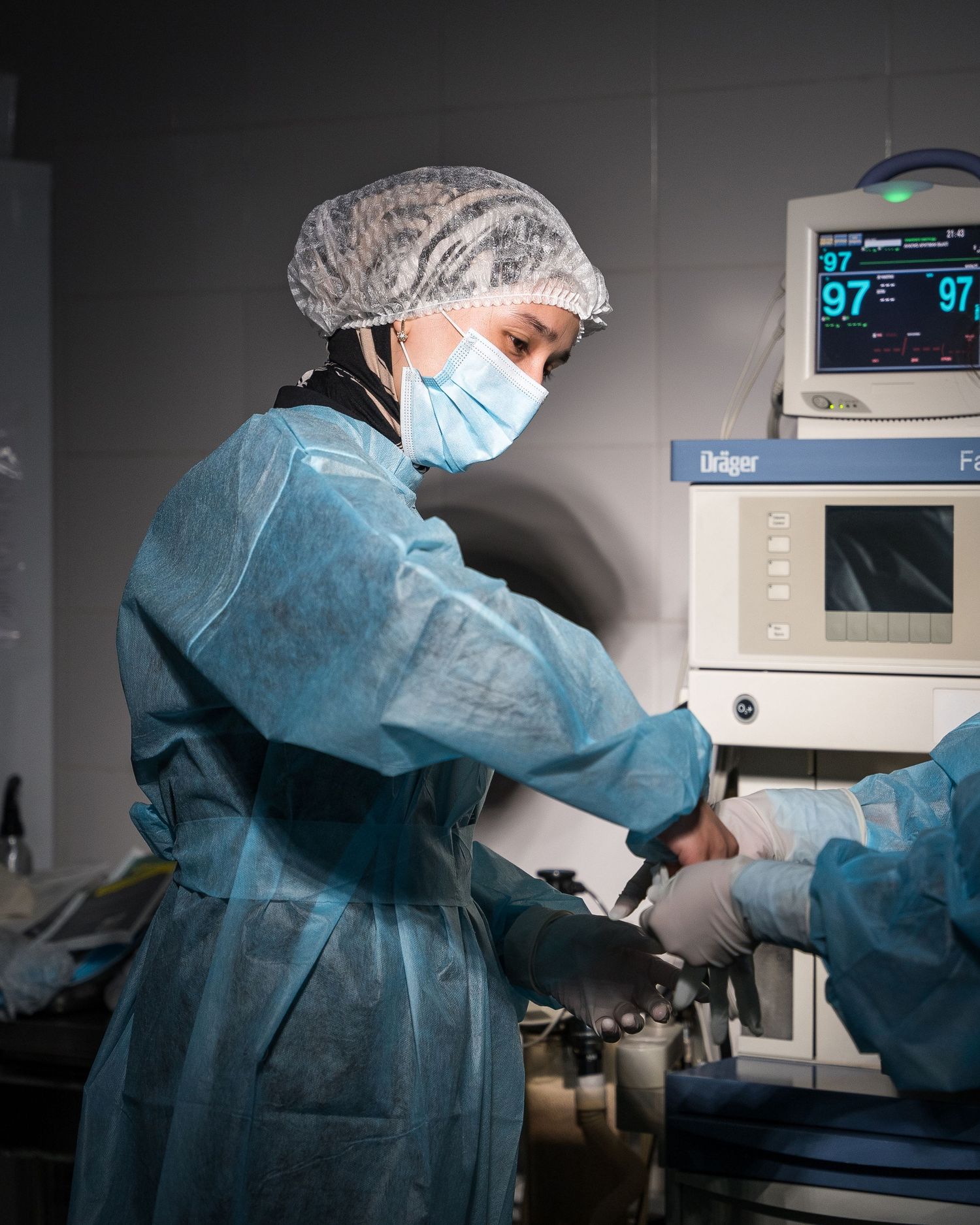 Medical team working in operating room with vital sign monitors visible in background.