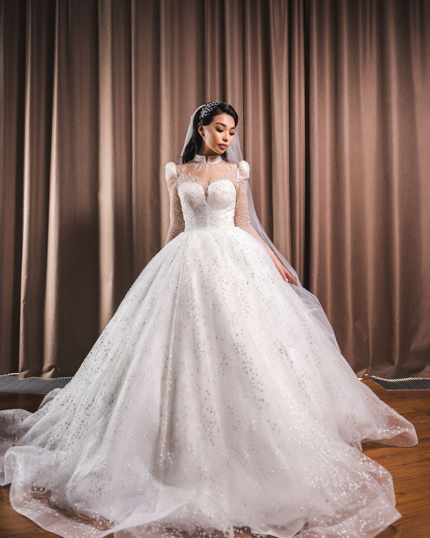 Bride in stunning sparkly ballgown wedding dress with sheer long sleeves and full skirt posing elegantly.