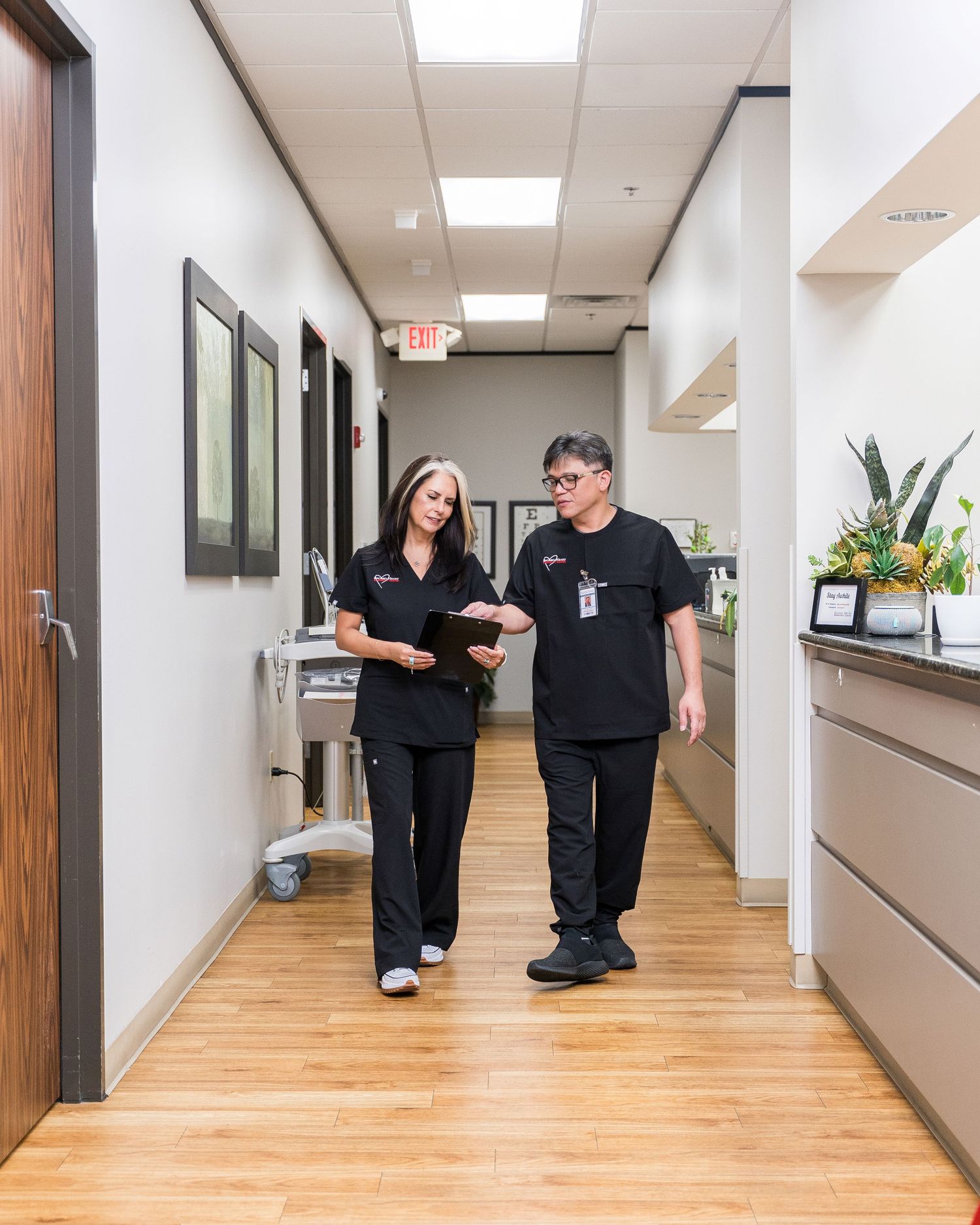 Medical staff in black scrubs interact in a modern healthcare facility hallway with wood flooring.
